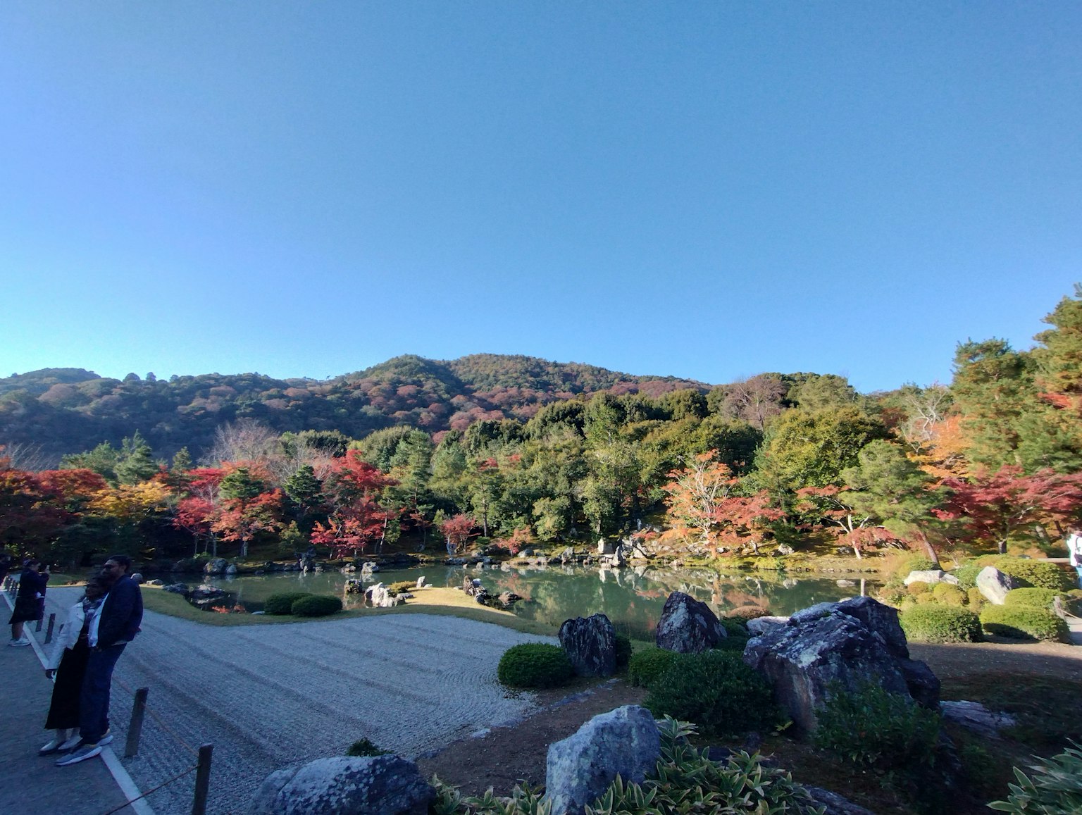 Beautiful autumn landscape in a garden with people strolling around a serene pond surrounded by colorful foliage