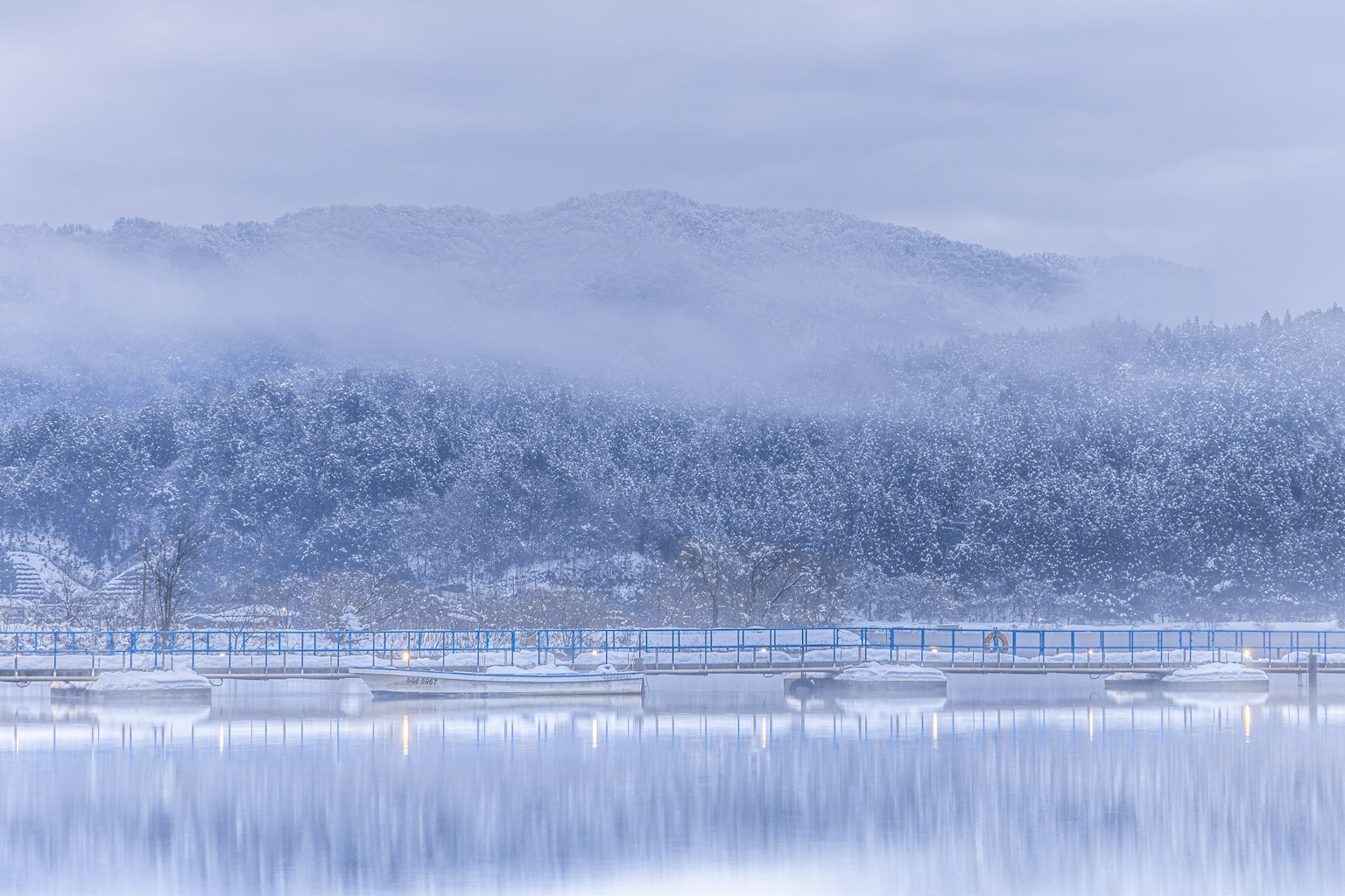 霧氣瀰漫的冬季景觀，雪覆蓋的山脈和寧靜的湖泊