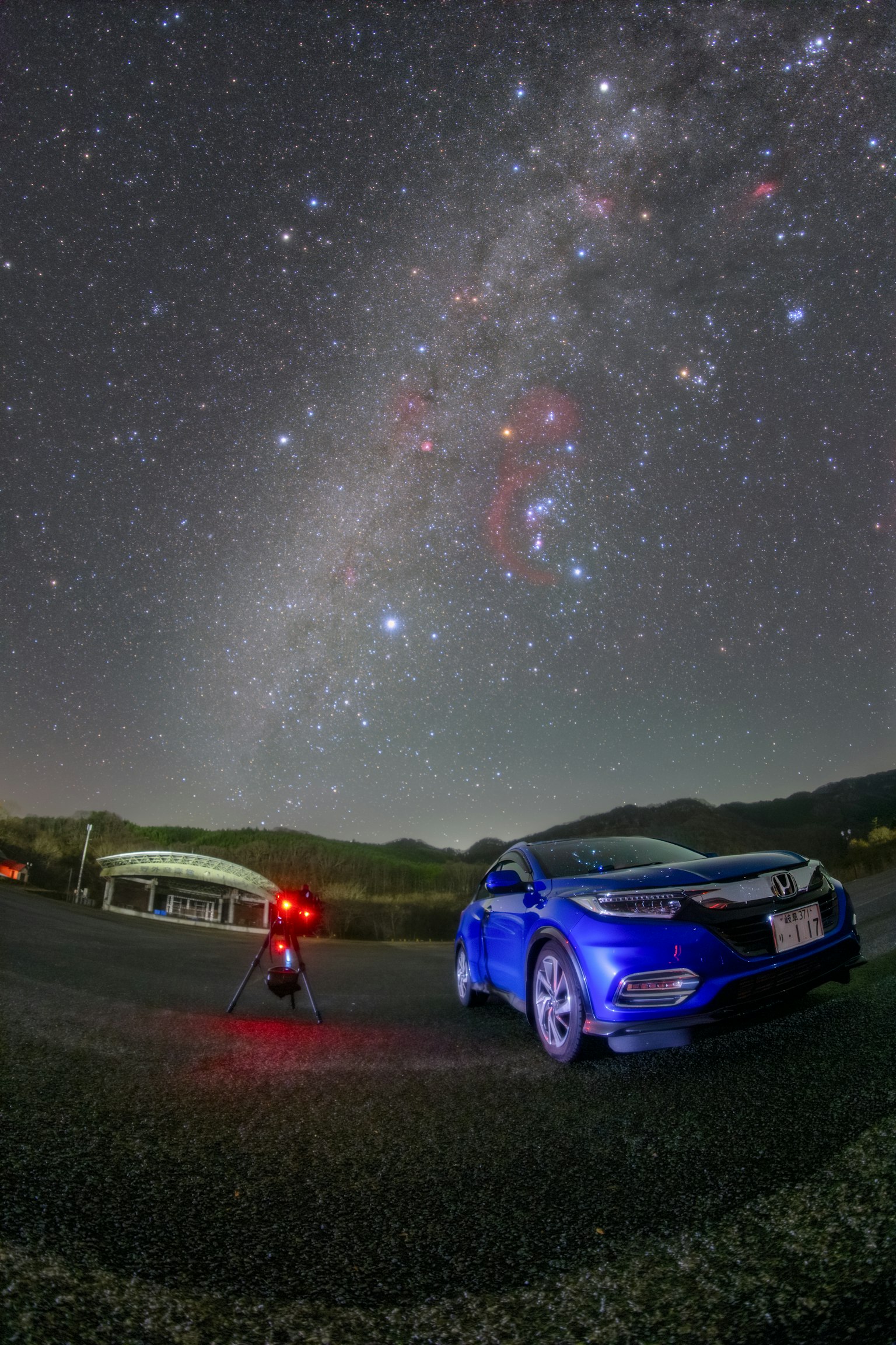 Une voiture bleue garée sous un ciel étoilé avec un photographe à proximité