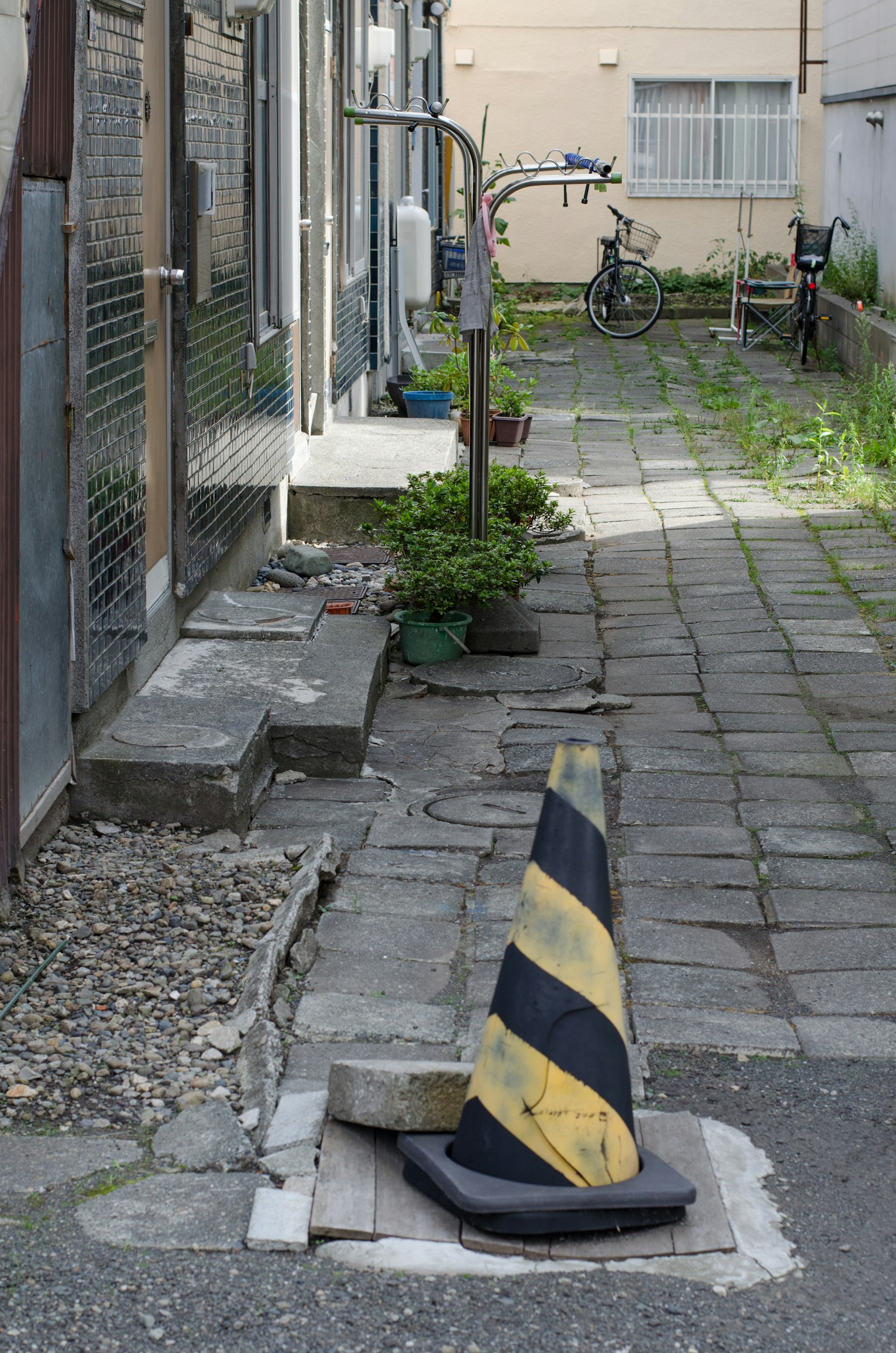 Cortile stretto con un cono stradale nero e giallo e piante
