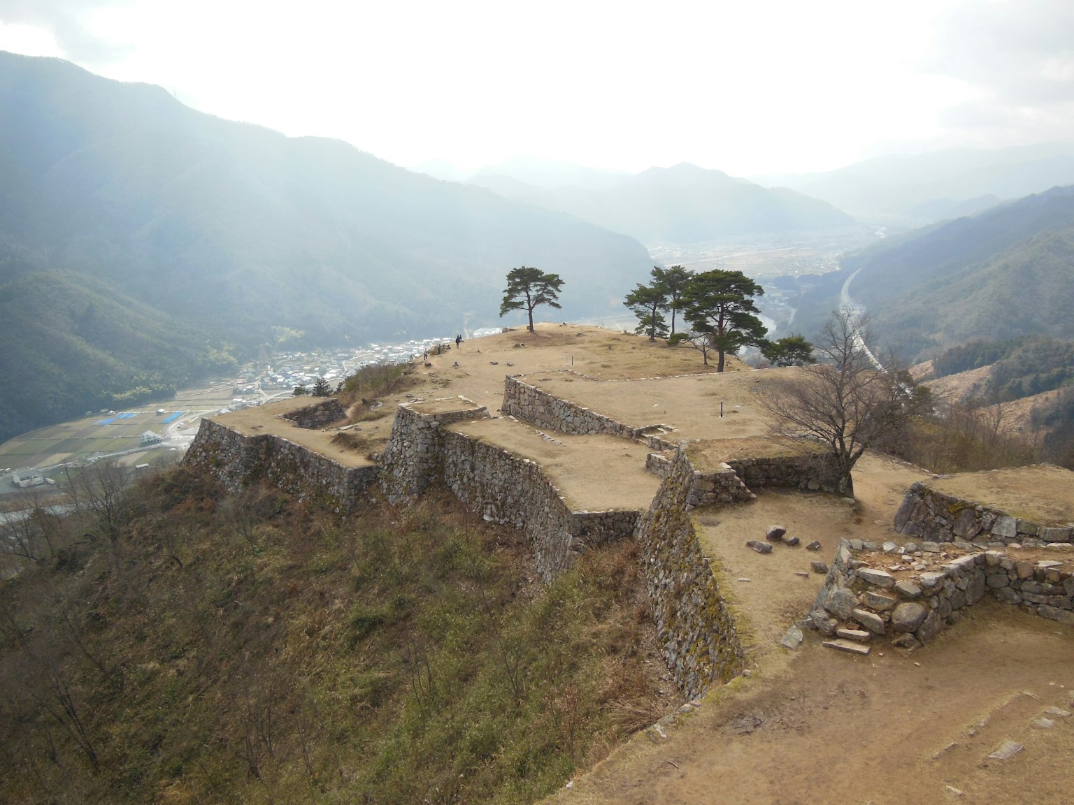 Ruines anciennes sur un plateau élevé avec des montagnes vertes et une rivière visible
