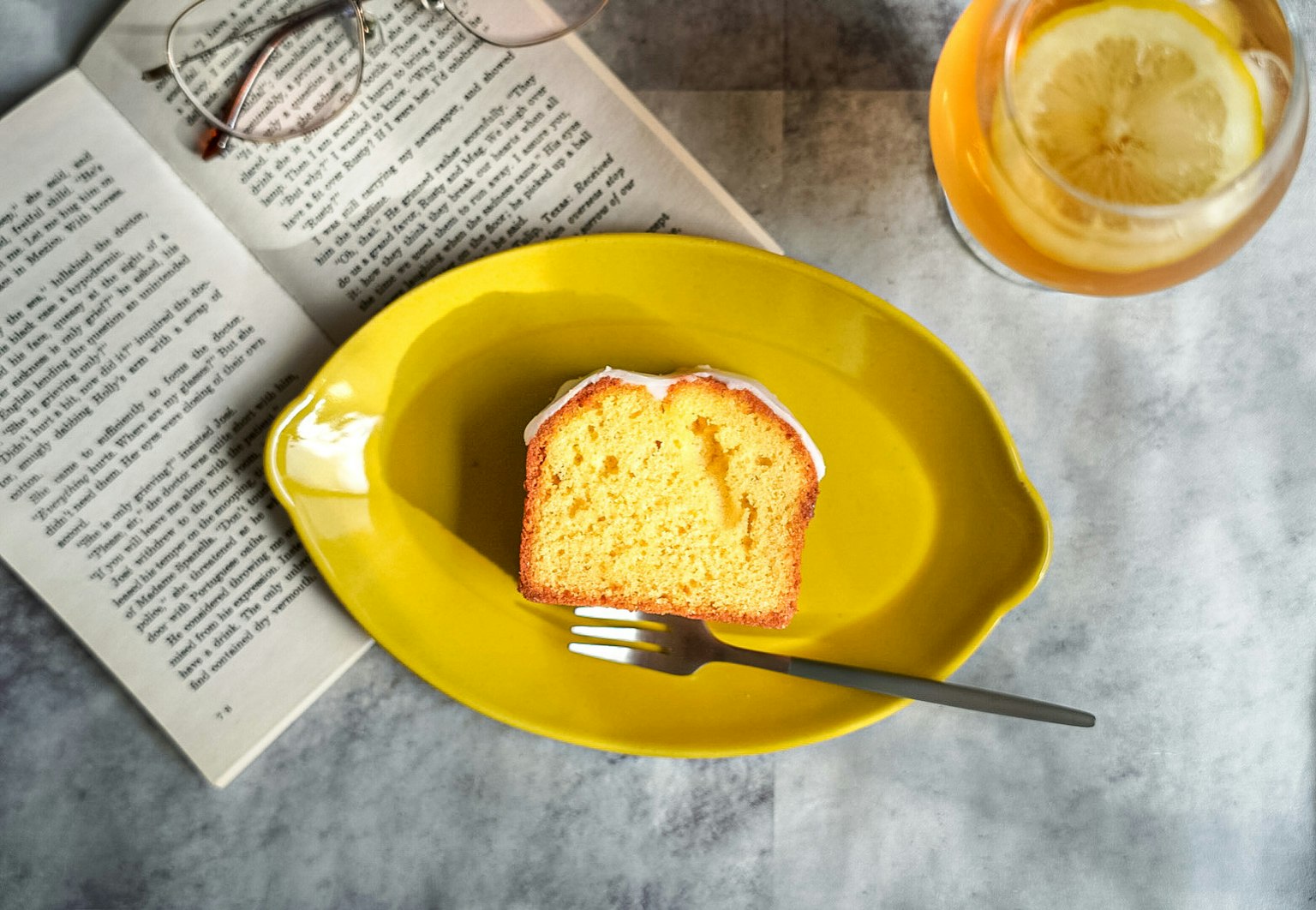 Una fetta di torta soffice su un piatto giallo con una forchetta Occhiali e una bevanda su un libro aperto