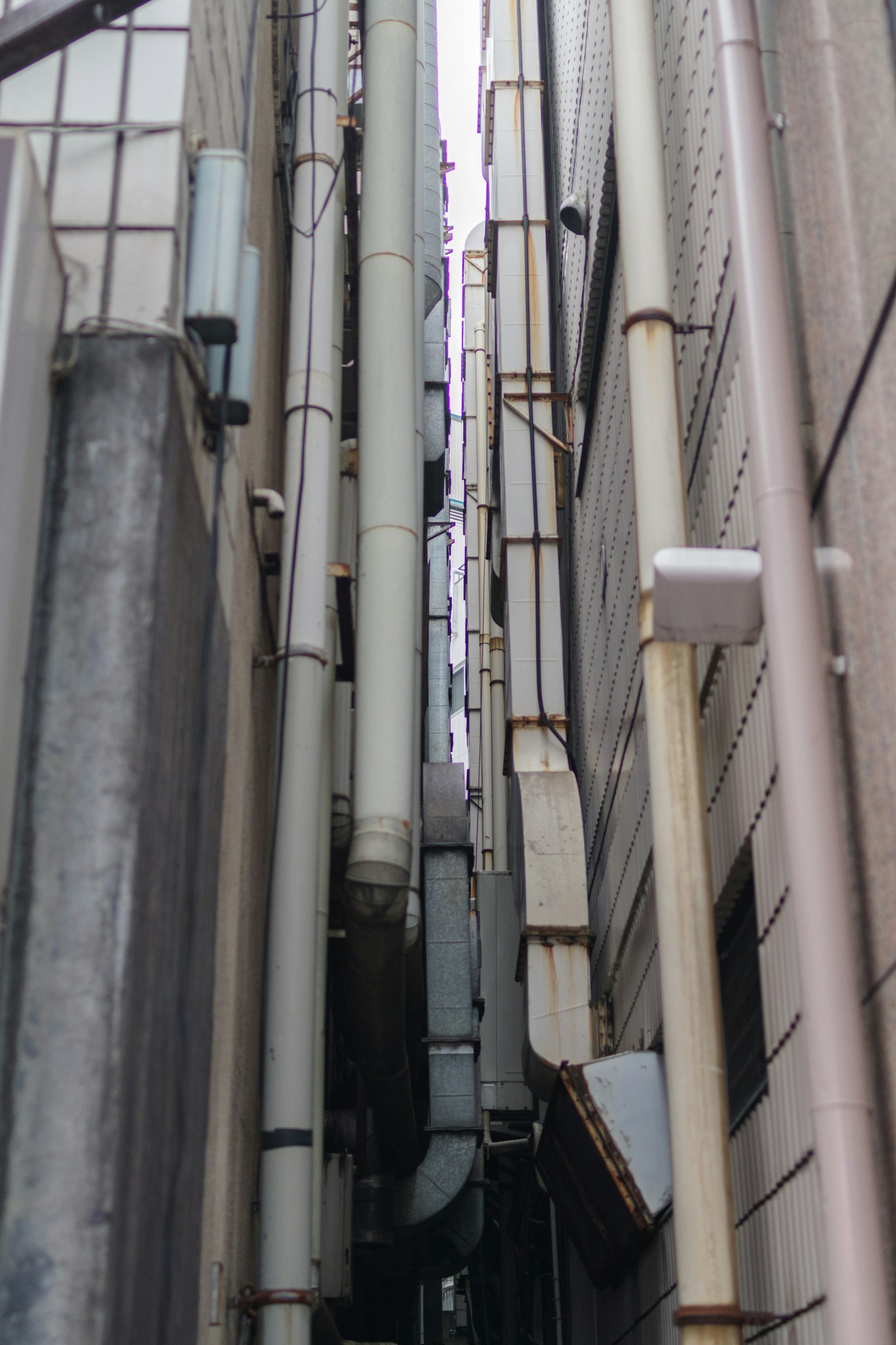 Callejón estrecho entre edificios que muestra tuberías y paredes