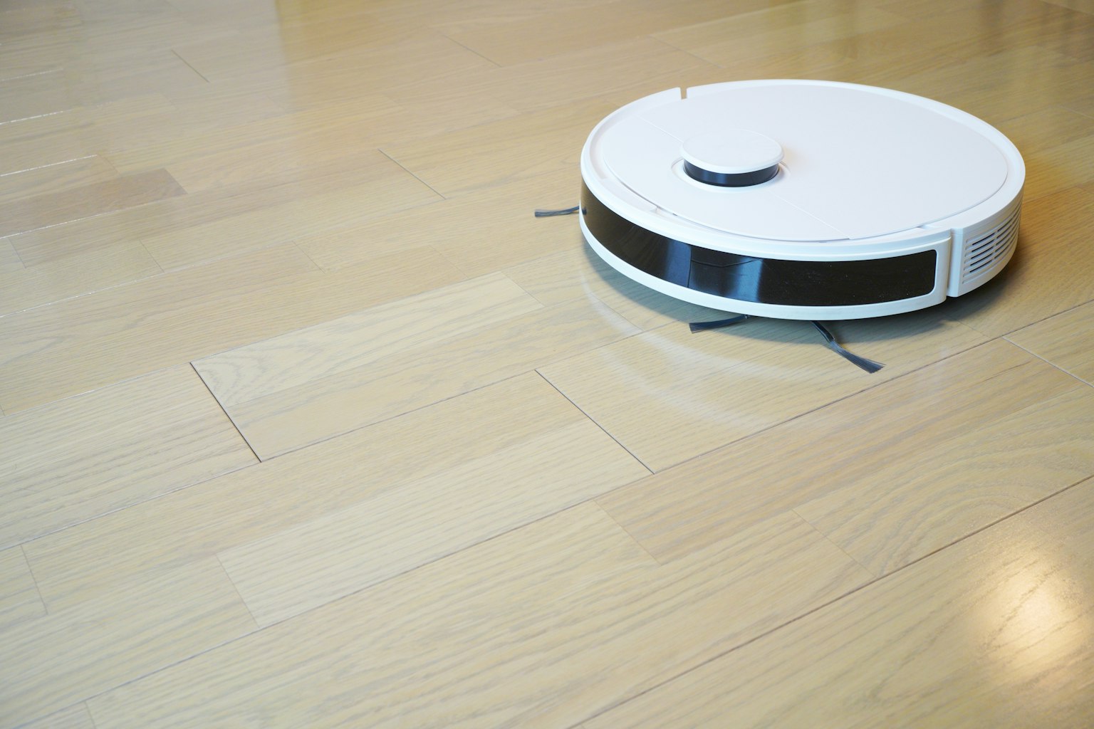Un robot aspirateur blanc se déplaçant sur un sol en bois