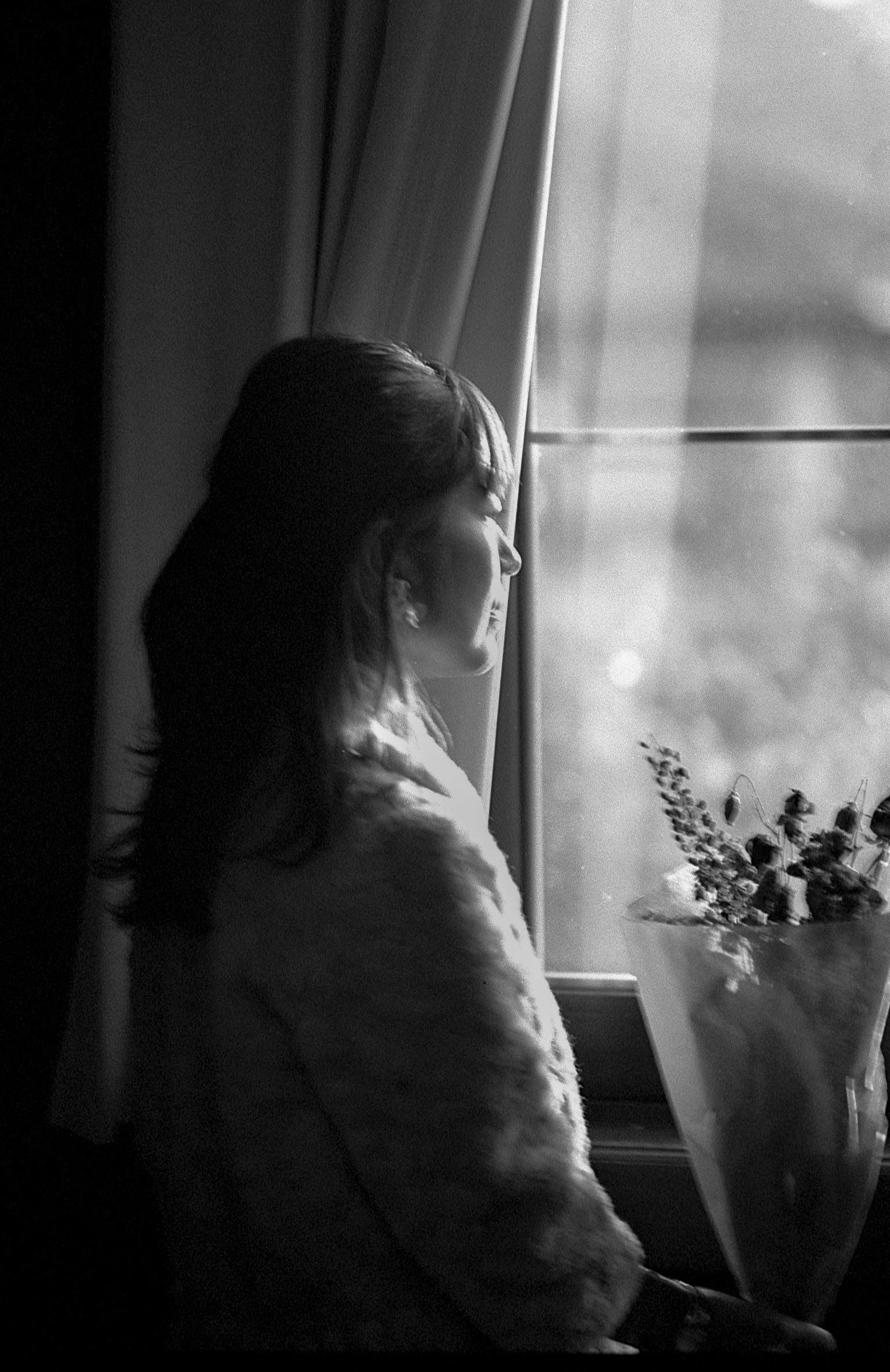 Photo en noir et blanc d'une femme debout près d'une fenêtre tenant un bouquet