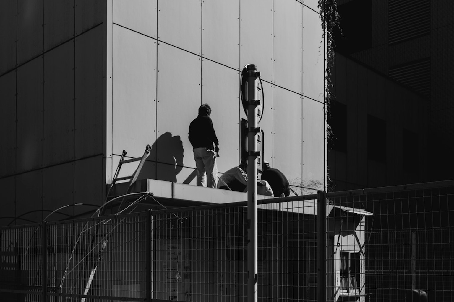 Schatten von Arbeitern an einer Gebäudefassade mit Glasreflexionen