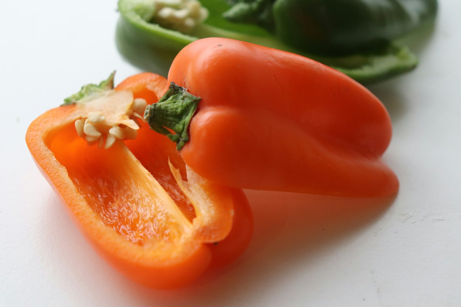 Un poivron orange coupé en deux avec des graines visibles à côté d'un poivron vert en arrière-plan