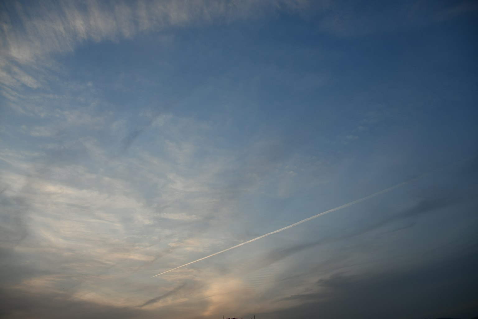 Ein blauer Himmel mit dünnen Wolken und einer Flugzeugspur