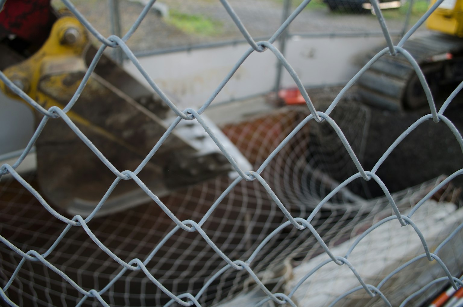Cucharón de excavadora y red vistos a través de una cerca de malla de alambre