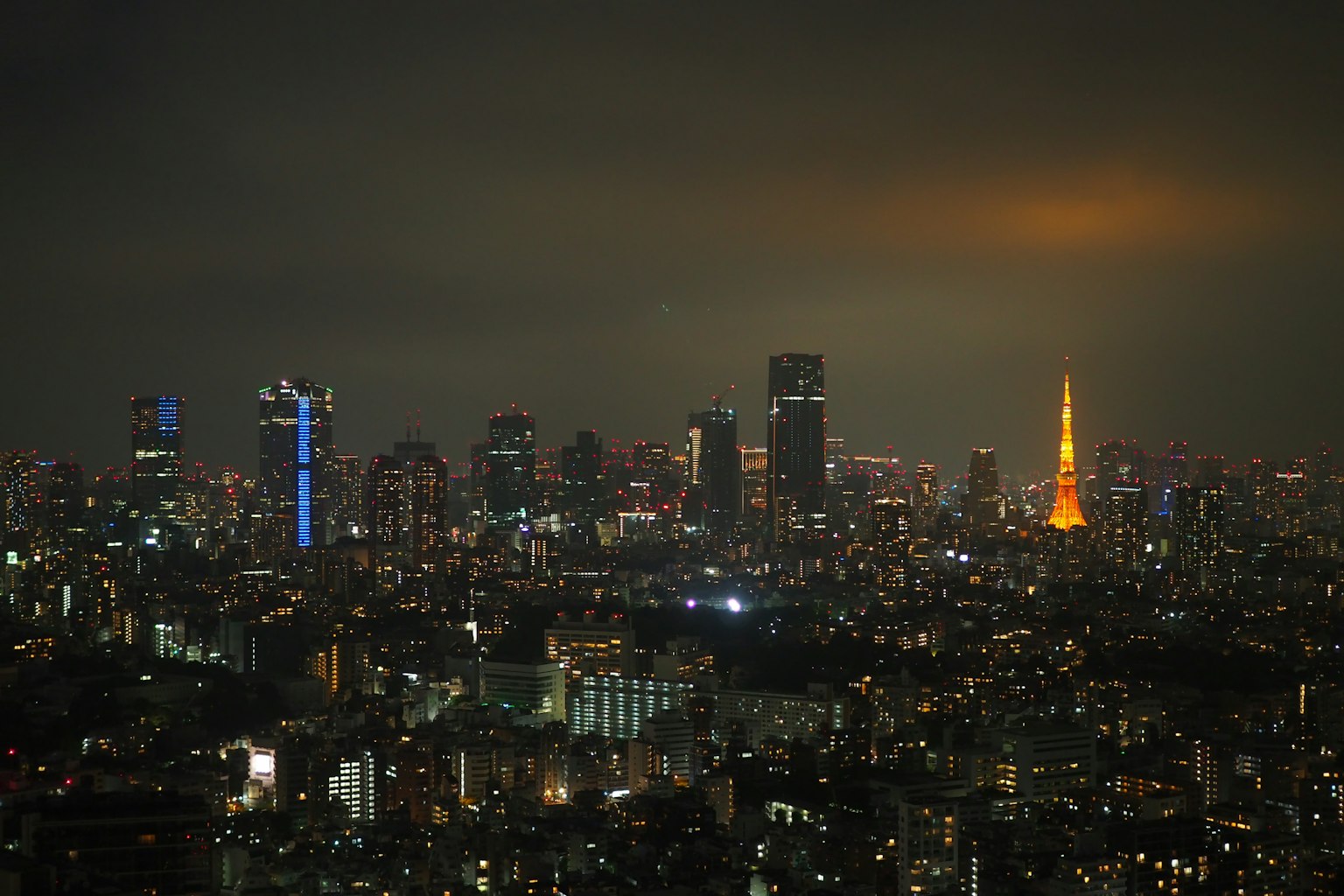 Tokyo skyline at night with bright tower and skyscrapers under cloudy sky