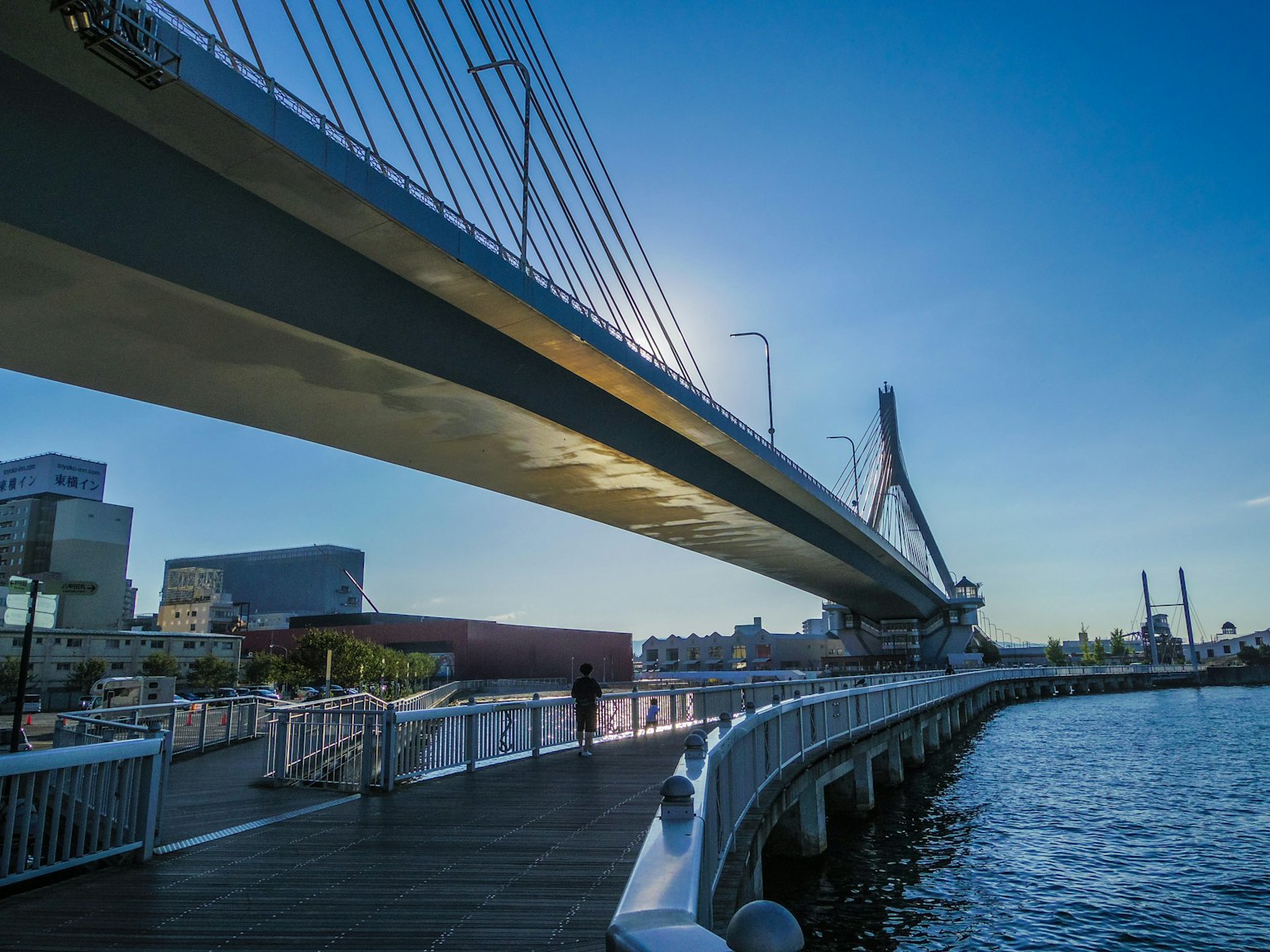 Pont moderne s'étendant sur l'eau avec une promenade et un ciel bleu