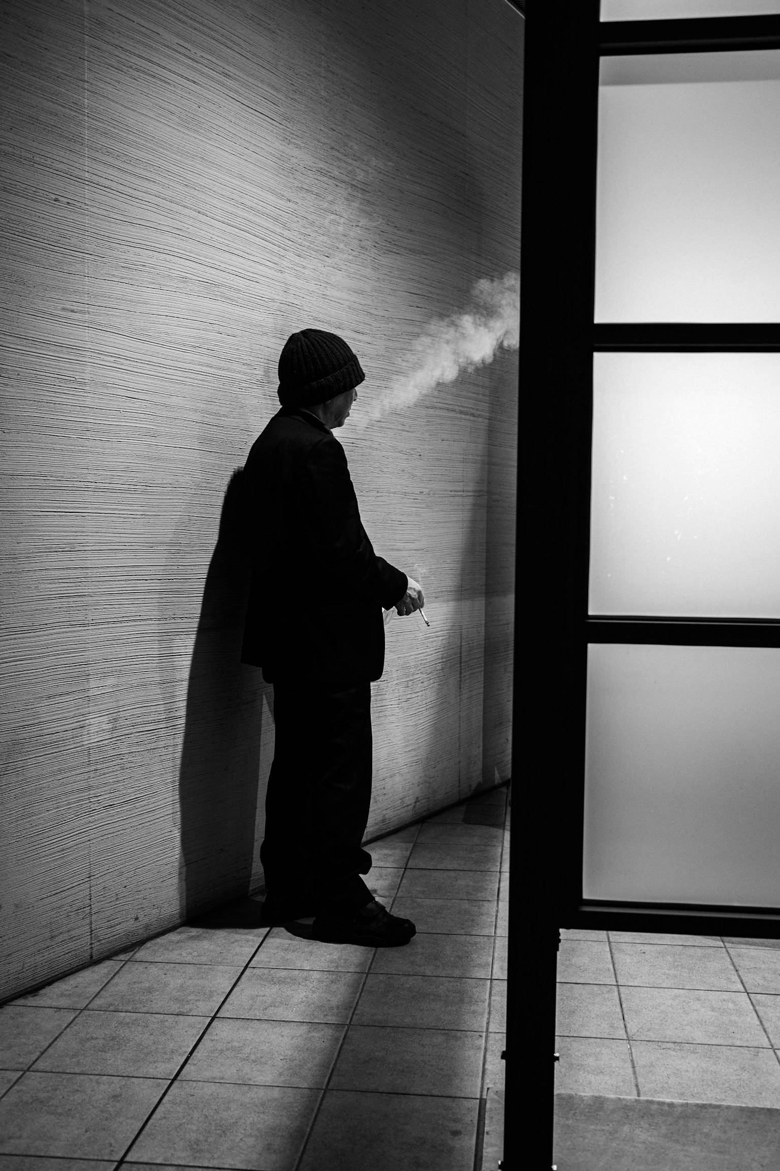Silhouette di un uomo che fuma contro un muro in bianco e nero