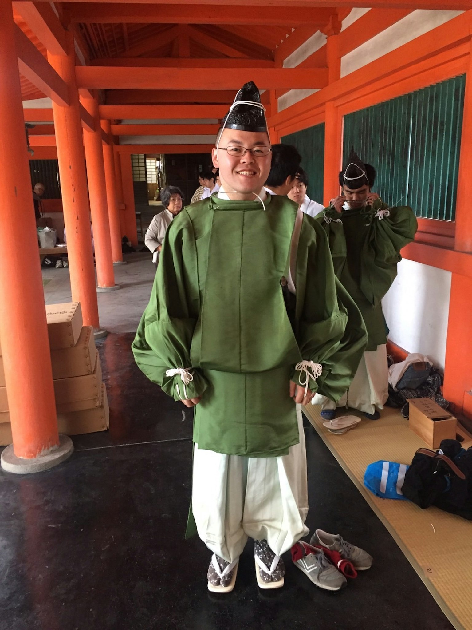 穿着传统绿色服装的微笑男性站在橙色柱子前