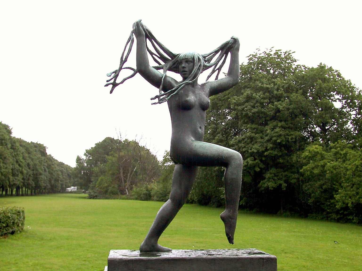 Una scultura di una donna che danza in un parco tenendo i capelli sollevati