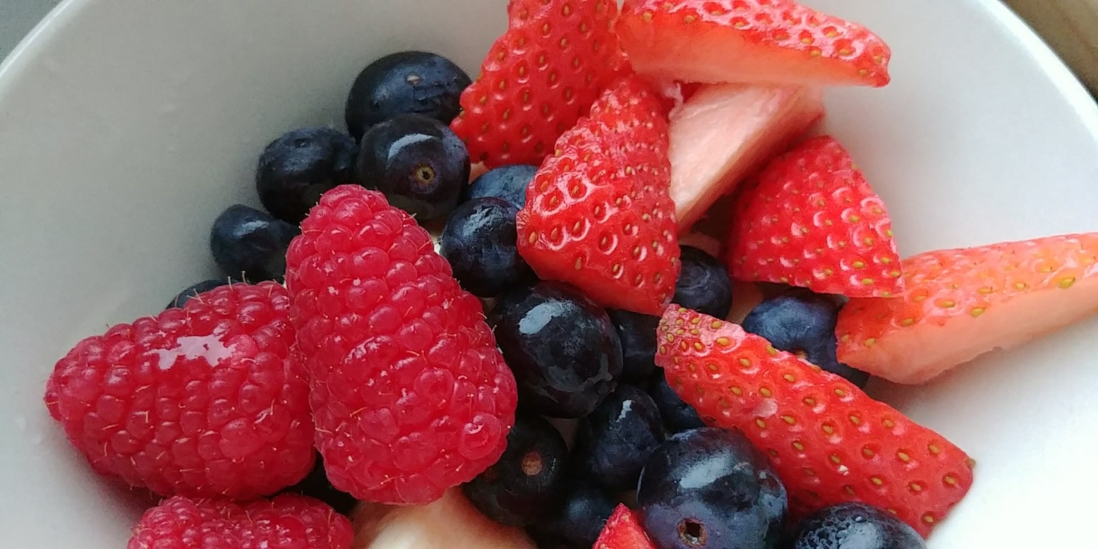 Fresh raspberries blueberries and strawberries in a white bowl