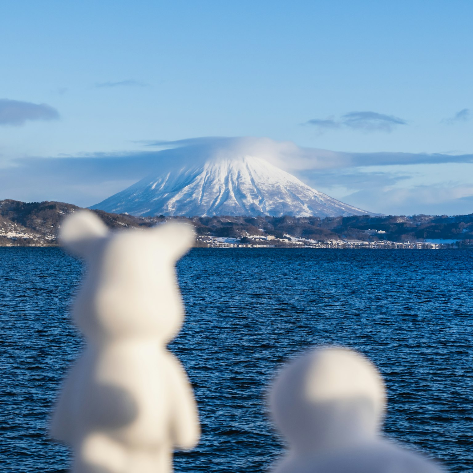 Two white bear figurines overlooking the ocean with a snow-capped mountain in the background