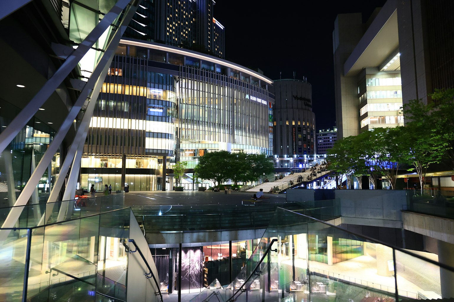 Night cityscape featuring large buildings and a glass plaza beautiful lighting and green trees