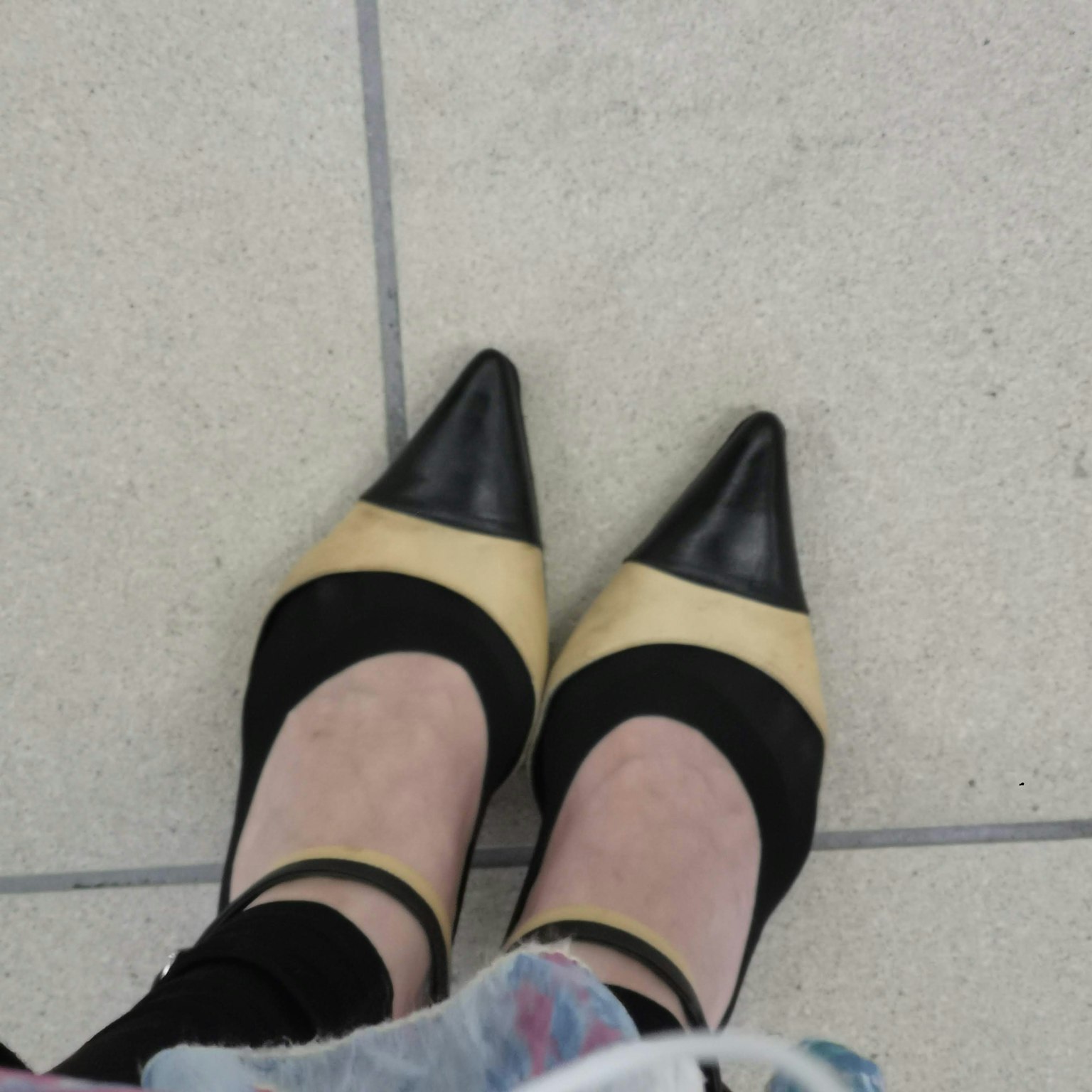 Nahaufnahme von schwarzen und beigen High Heels auf einem gefliesten Boden