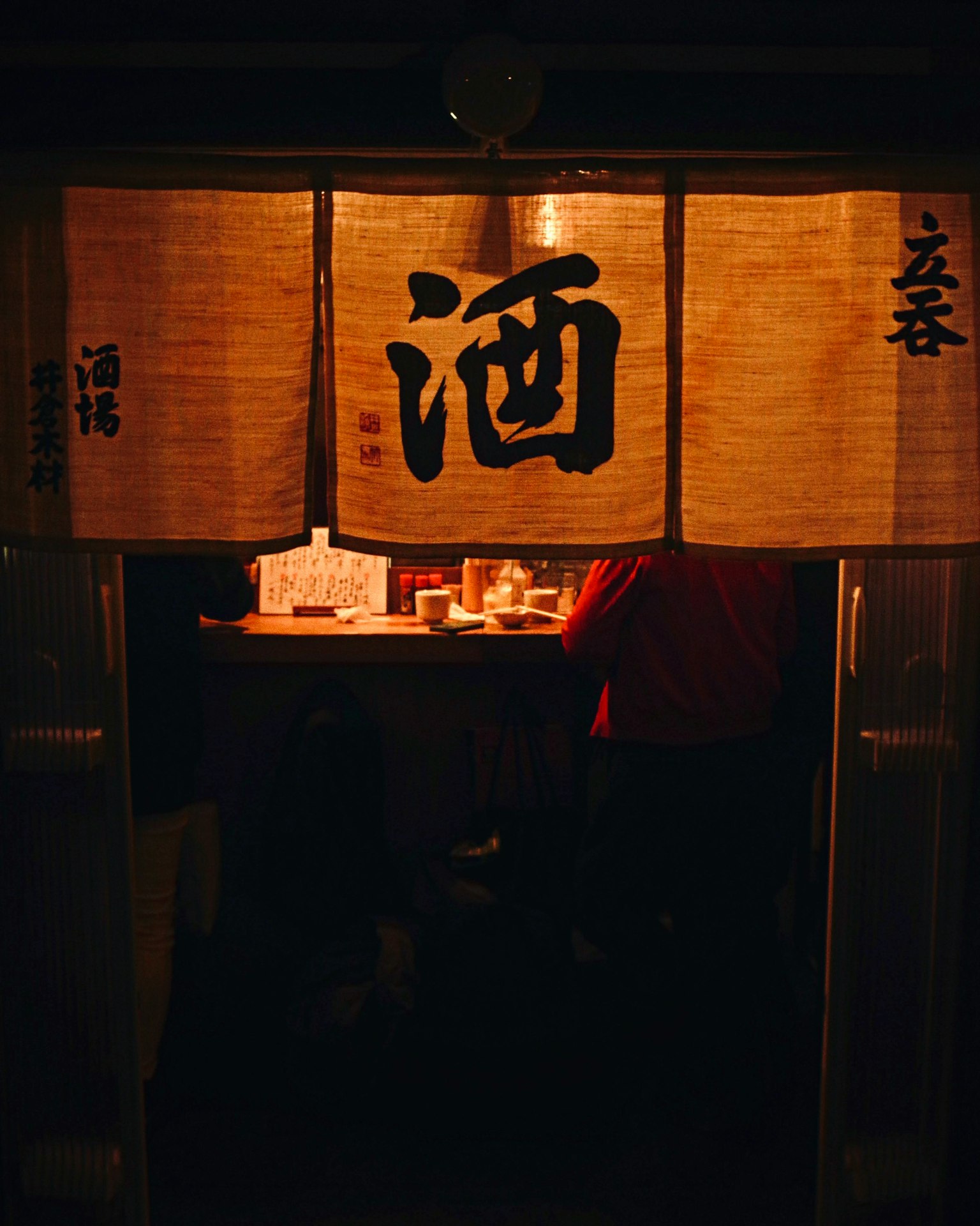 Entrance of a sake shop with warm-colored noren curtains displaying the character for sake