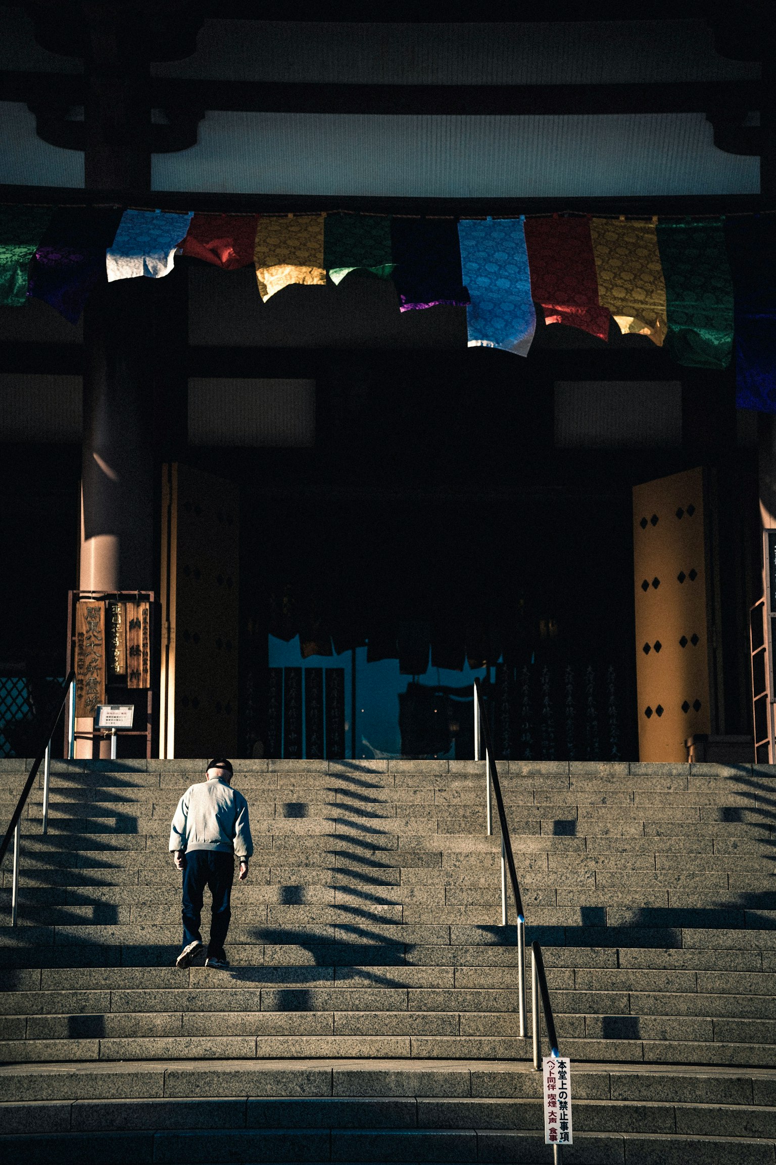 Person descending stairs at temple entrance with colorful prayer flags hanging