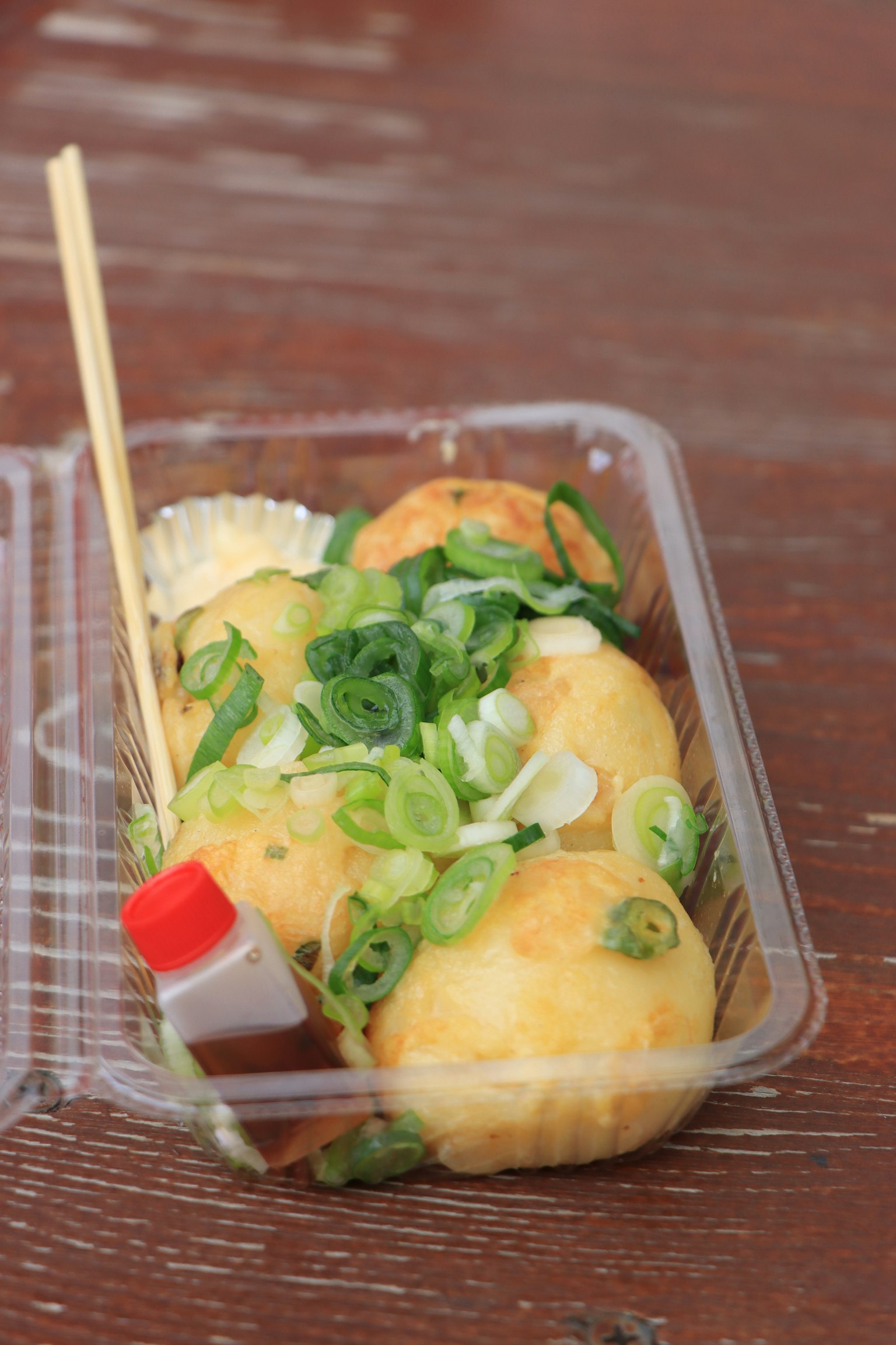 Takoyaki servi avec des oignons verts et de la sauce dans un récipient