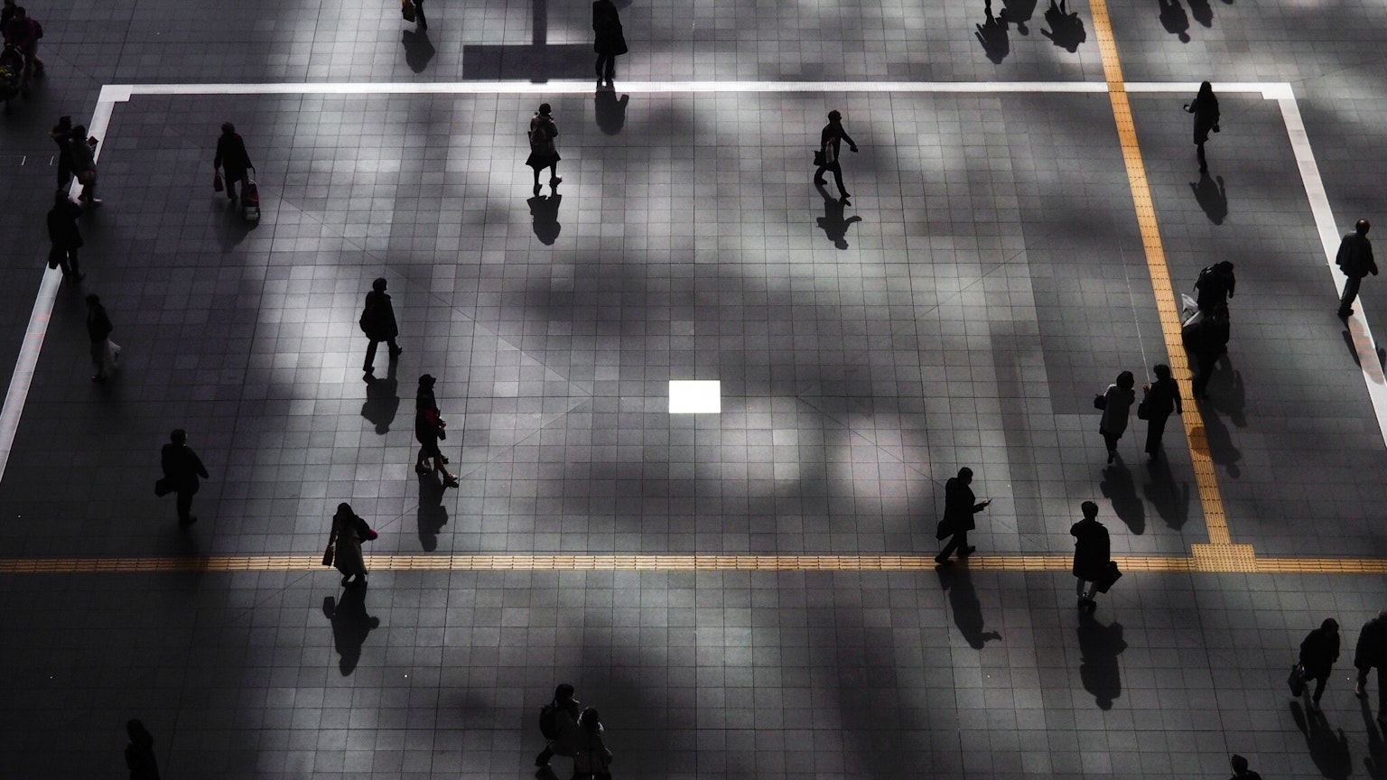 Vista aerea di una piazza cittadina con persone che camminano ombre e contrasto di luce