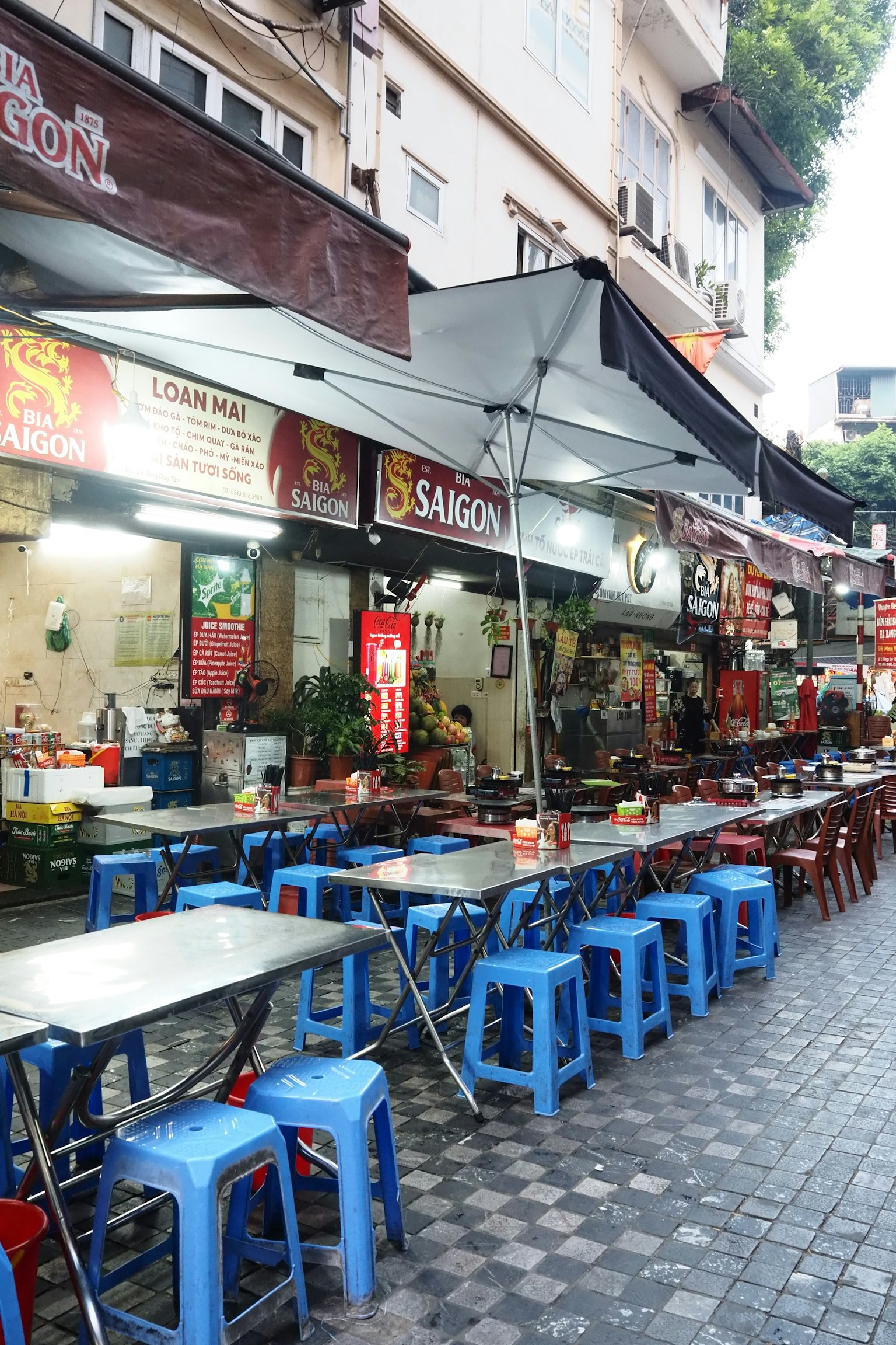 Escena de comida callejera en Vietnam con sillas y mesas azules y letreros de tiendas visibles