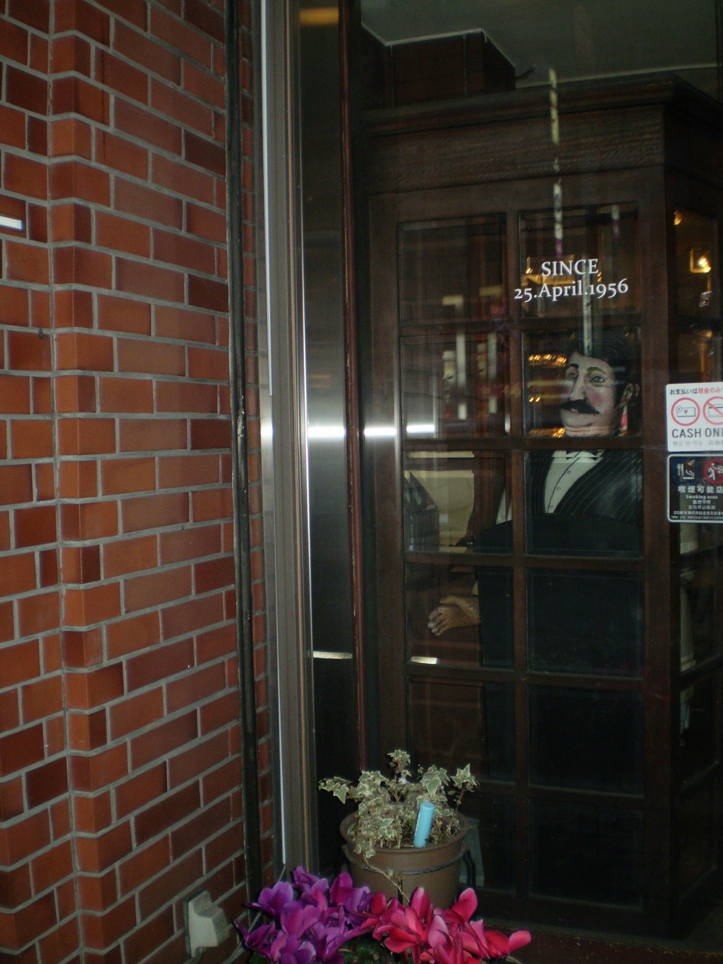 レンガ壁の入口に飾られた花とガラス越しの店内