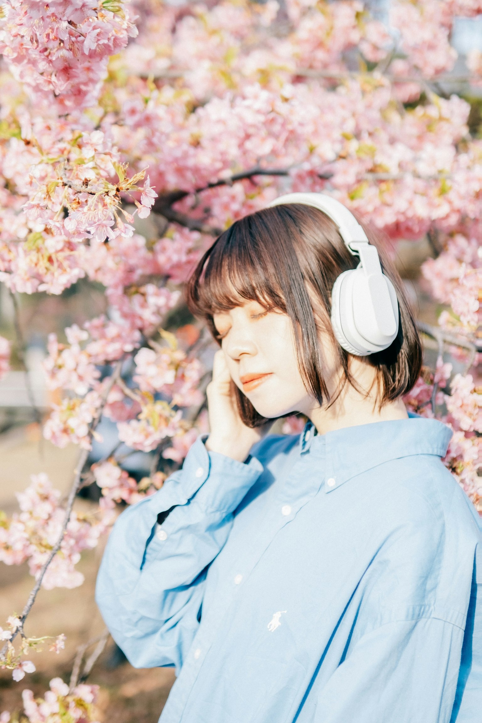 Woman wearing headphones in front of cherry blossoms