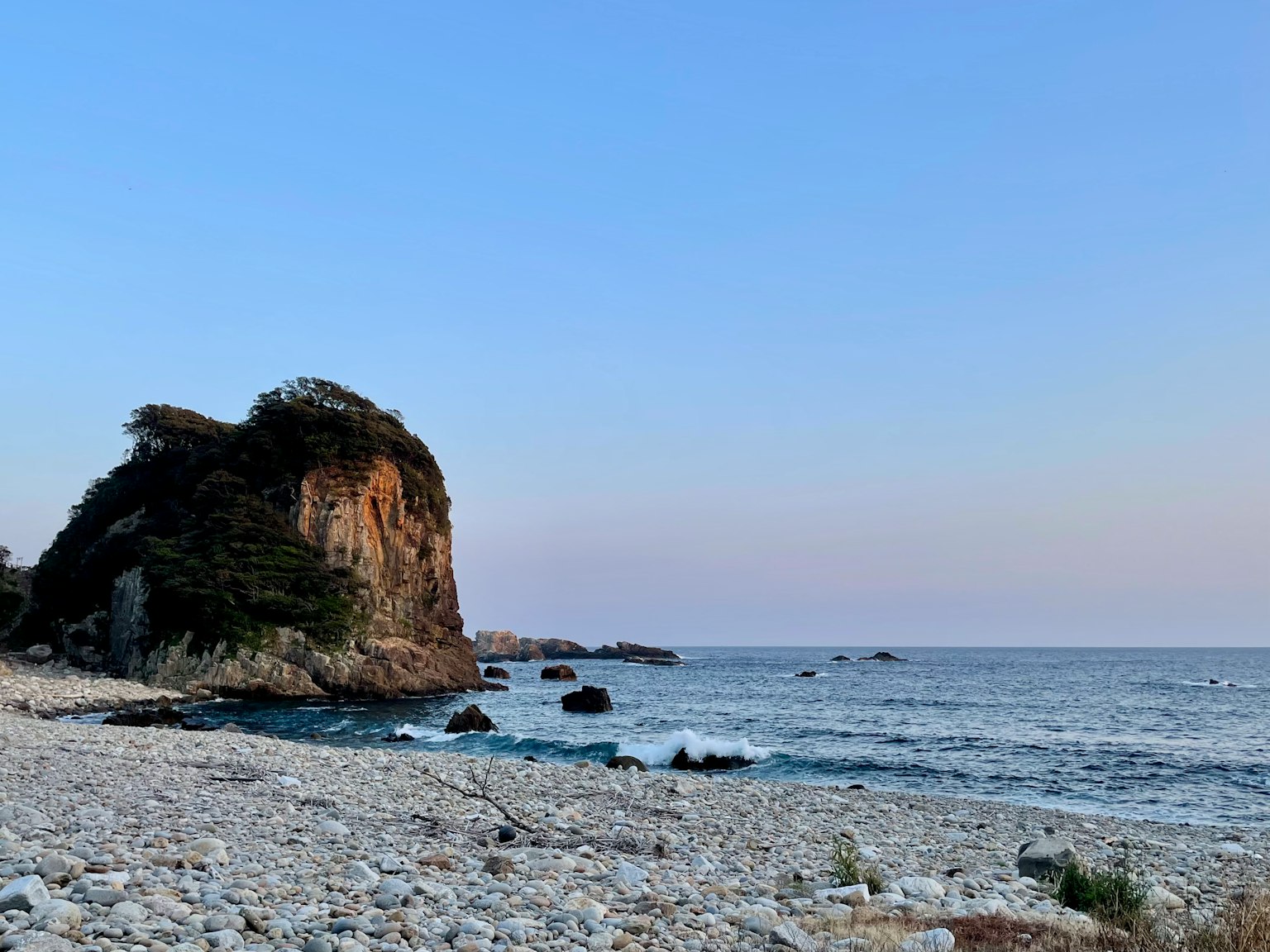 Vista costiera con una spiaggia rocciosa e cielo sereno al crepuscolo