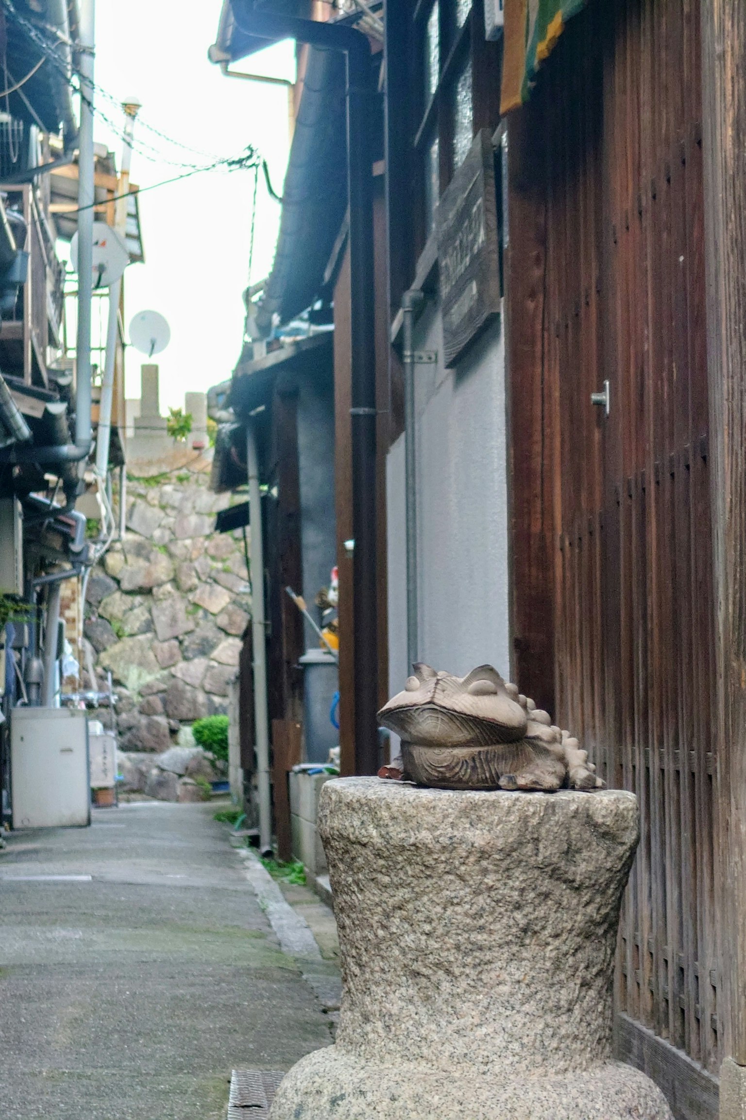 Une sculpture de grenouille sur un piédestal en pierre dans une ruelle étroite