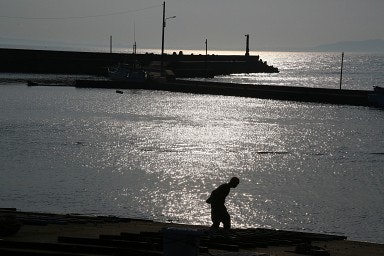 夕暮れの海辺で立つ老人と波打ち際の港