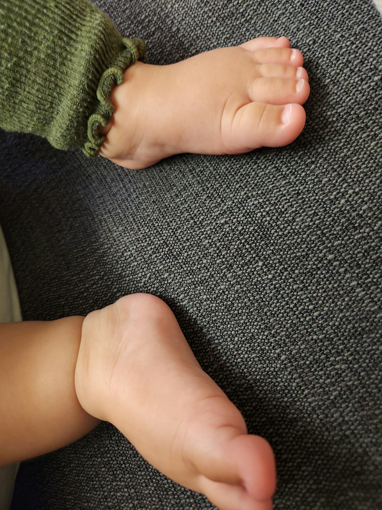 Dua kaki bayi beristirahat di permukaan abu-abu yang berpola dengan lengan rajutan hijau terlihat