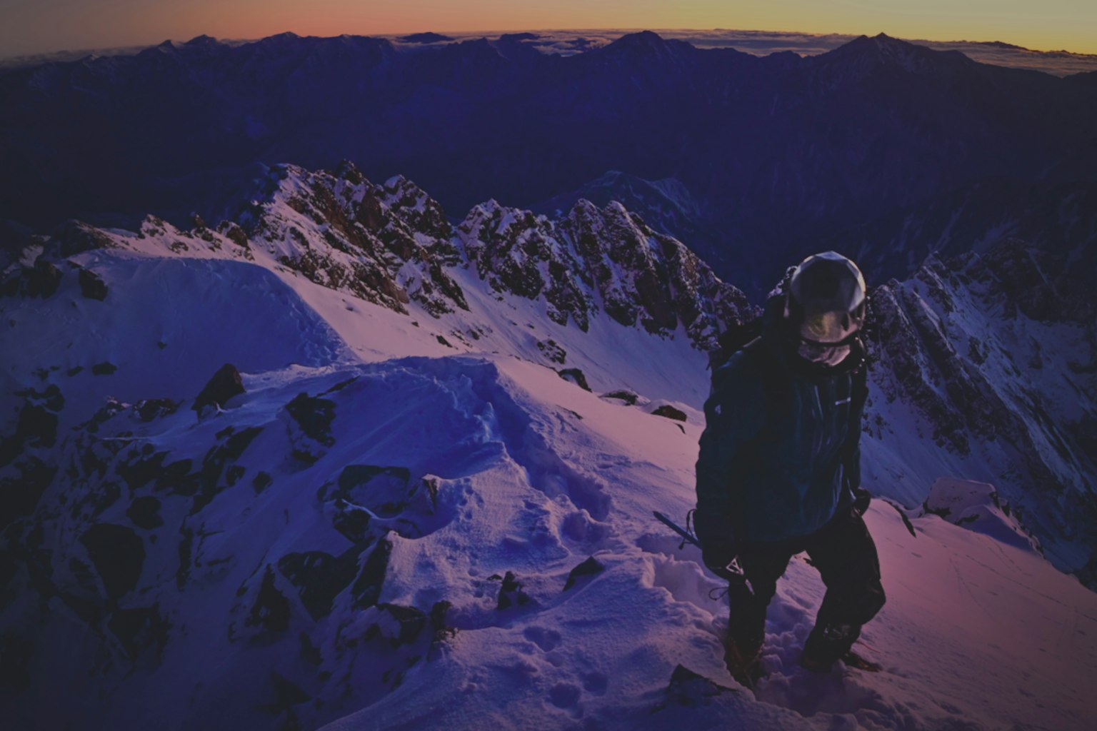 登山者在雪山顶峰上行走，夕阳下的美丽色调