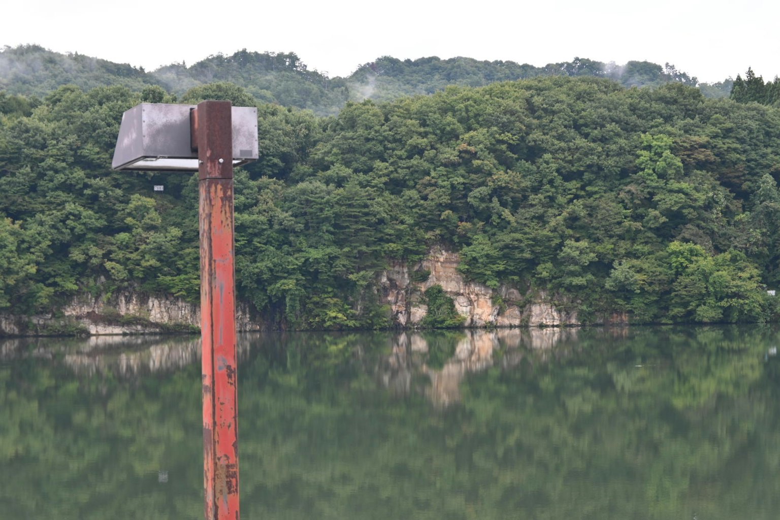 Reflejos de colinas verdes en un lago con un poste rojo en primer plano