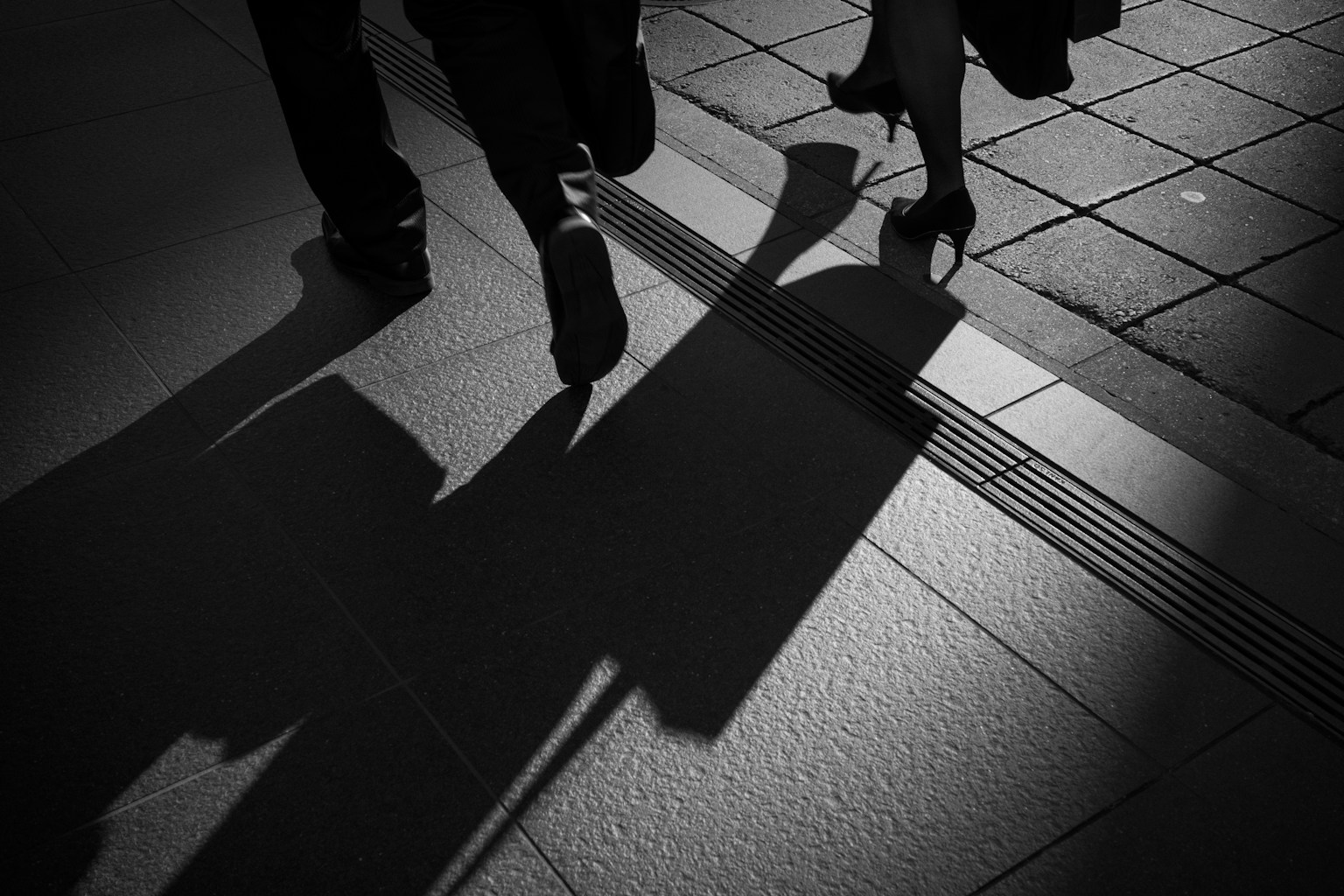 Siluet orang berjalan dengan sepatu hak tinggi dan bayangan di trotoar