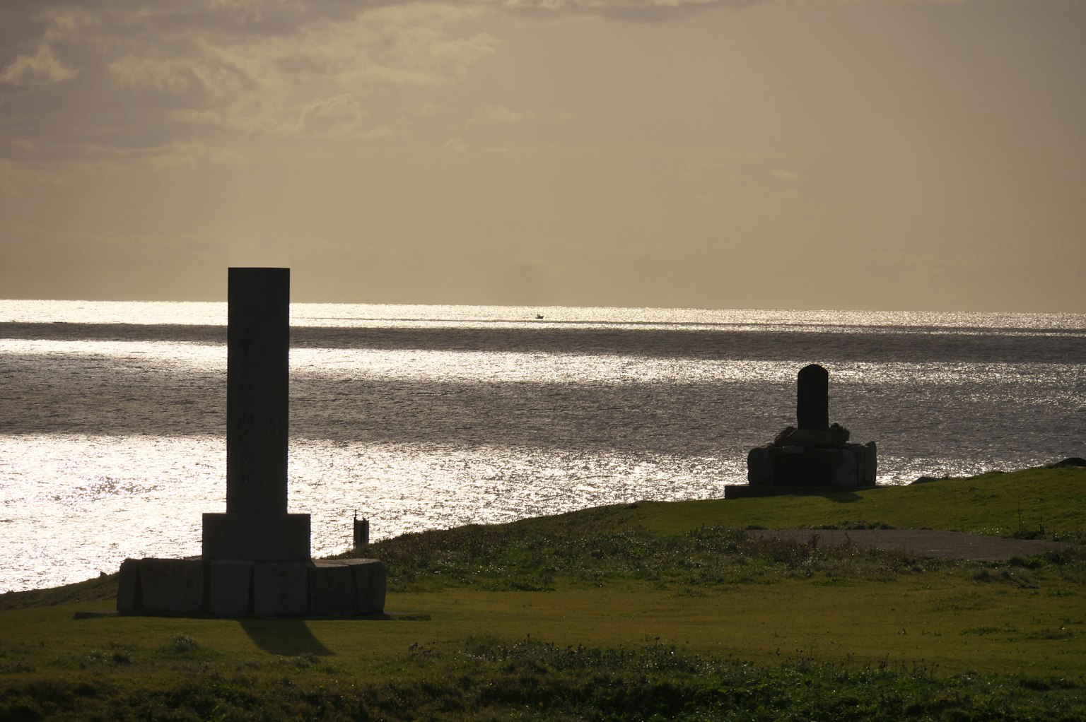 Due sculture di pietra su terreno erboso che si affacciano sul mare al tramonto