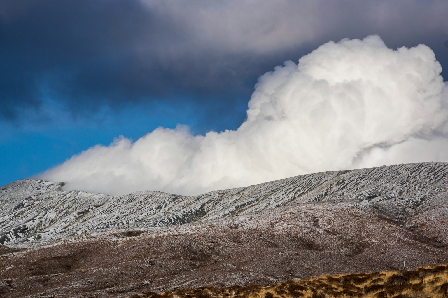 Schneebedeckter Berg mit flauschigen weißen Wolken vor blauem Himmel