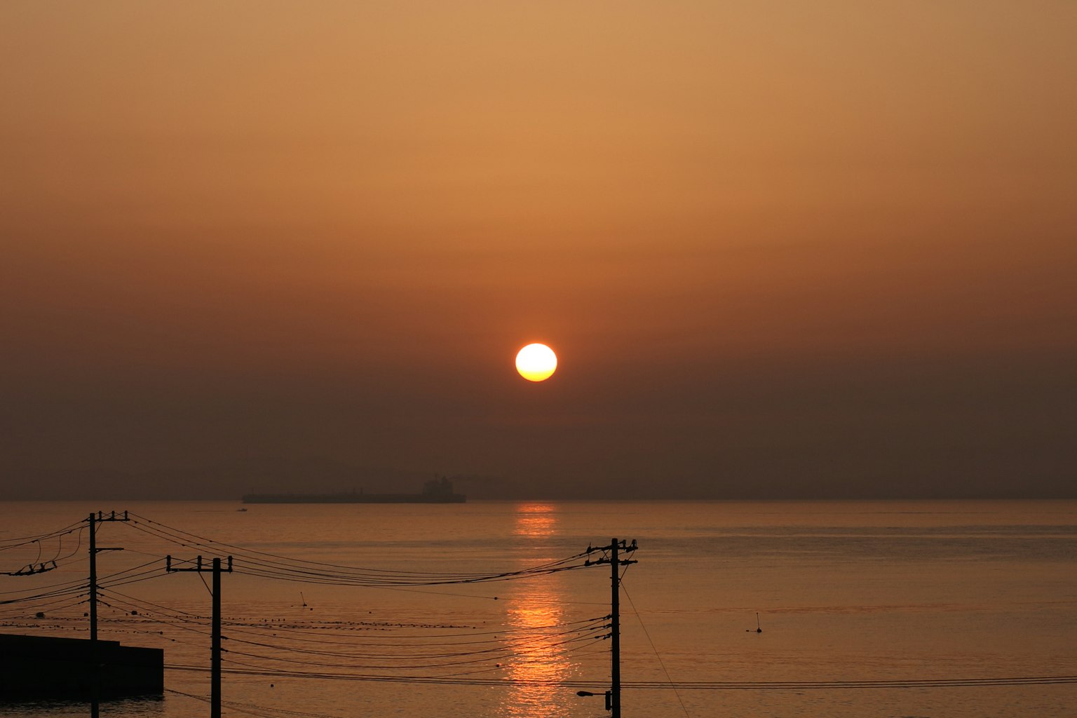Beautiful sunset over the sea with reflections on calm water and power lines