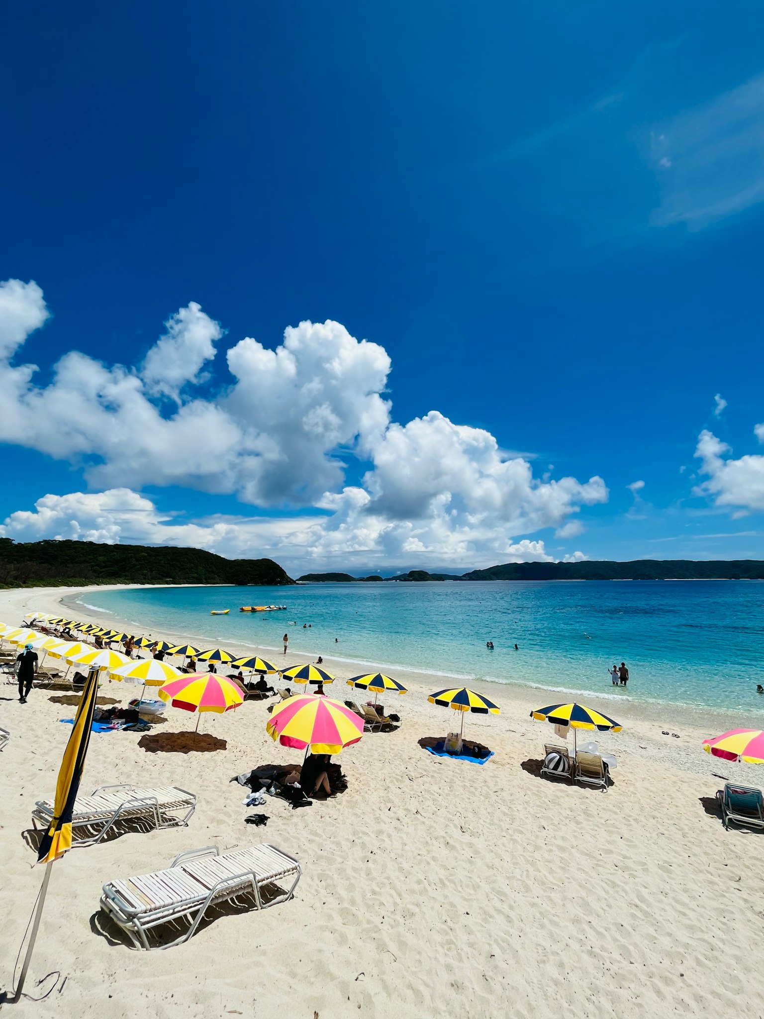 A beach with vibrant umbrellas and sun loungers on white sand beside a clear blue sea