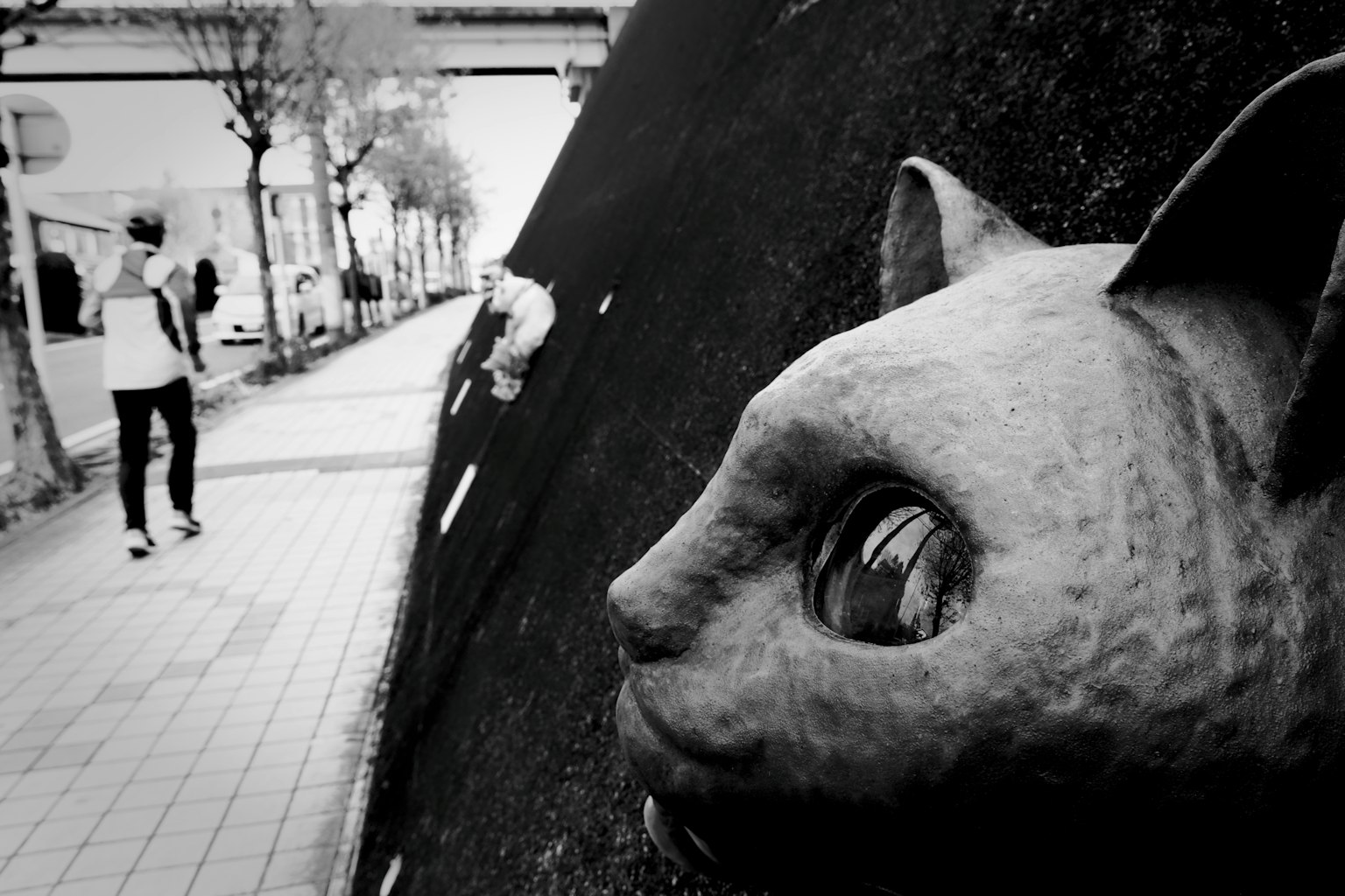 A cat sculpture on a black background with a passerby walking