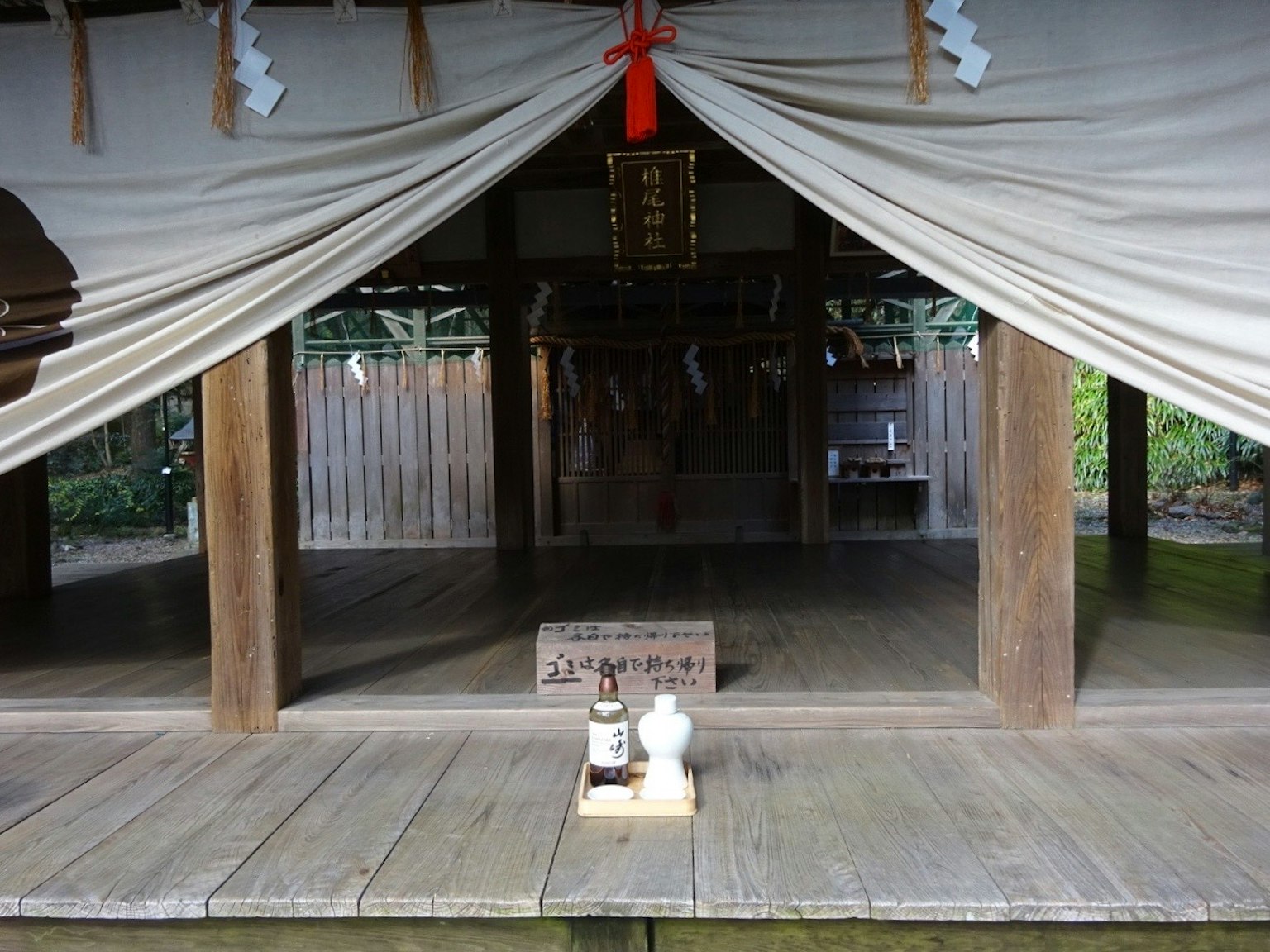 神社の内部が見える静かな風景で、中央にお供え物が置かれている
