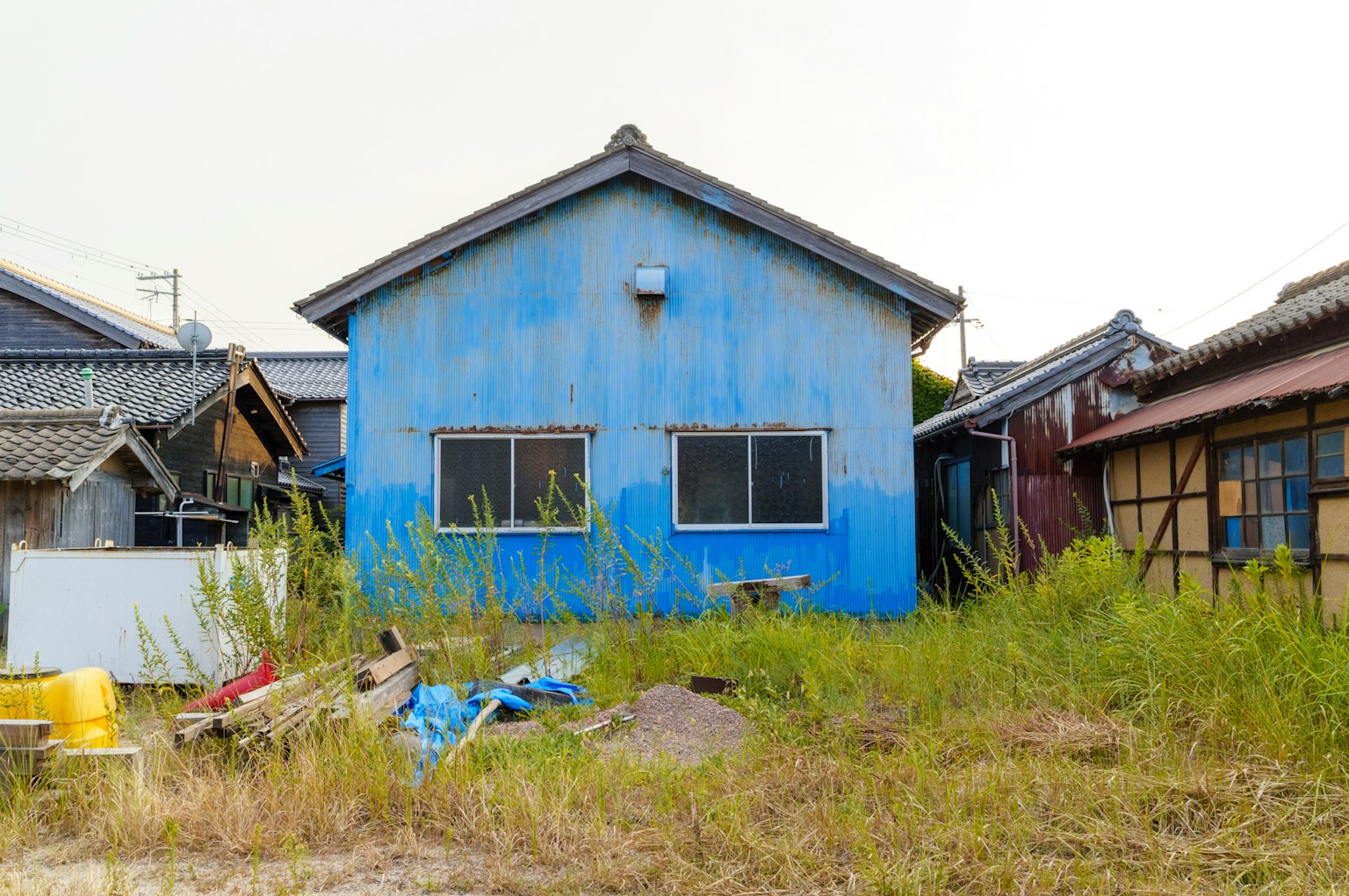Rumah tua dengan eksterior biru dikelilingi oleh rumput tinggi