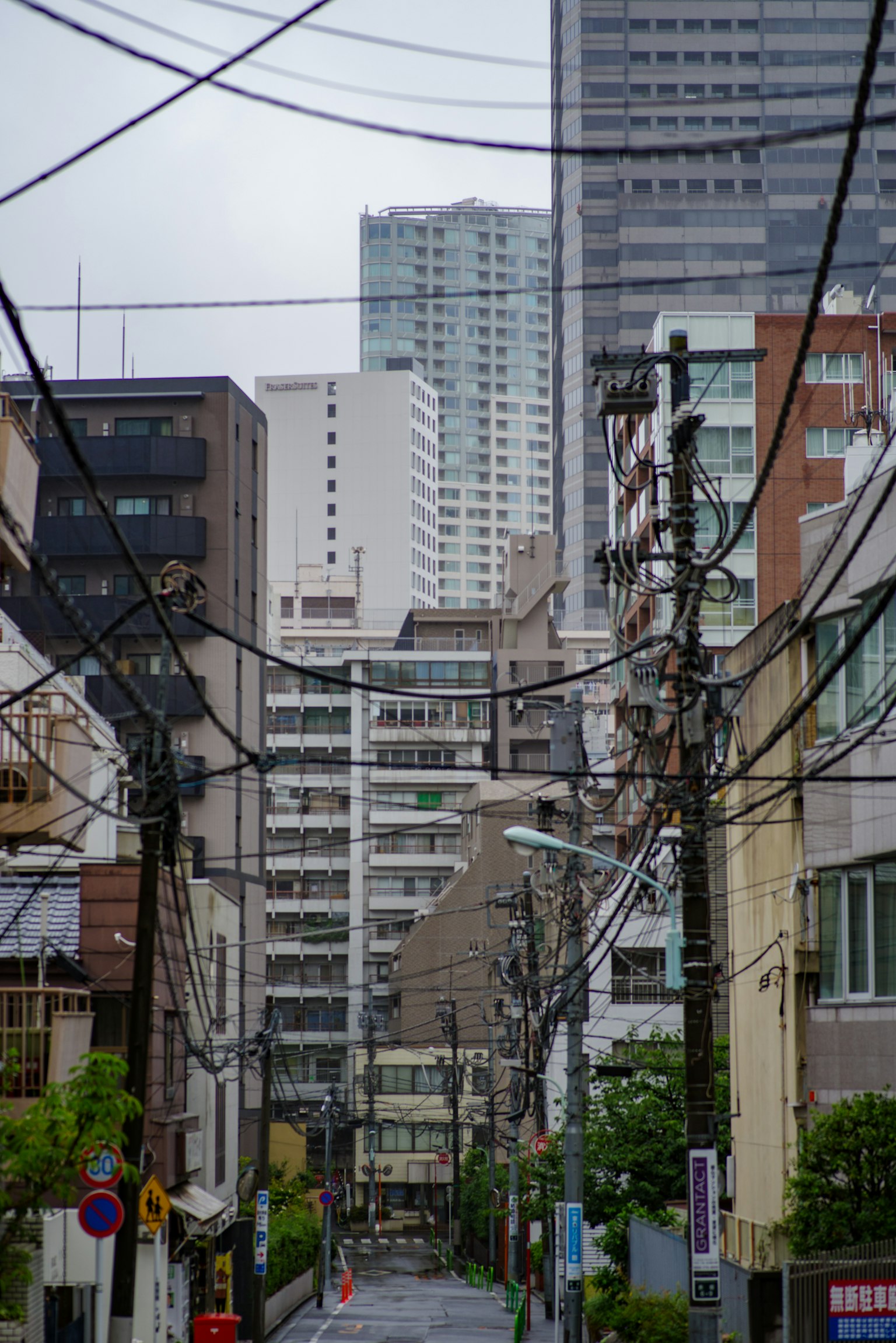 Scène de rue étroite à Tokyo avec des bâtiments résidentiels et des gratte-ciel visibles avec des lignes électriques