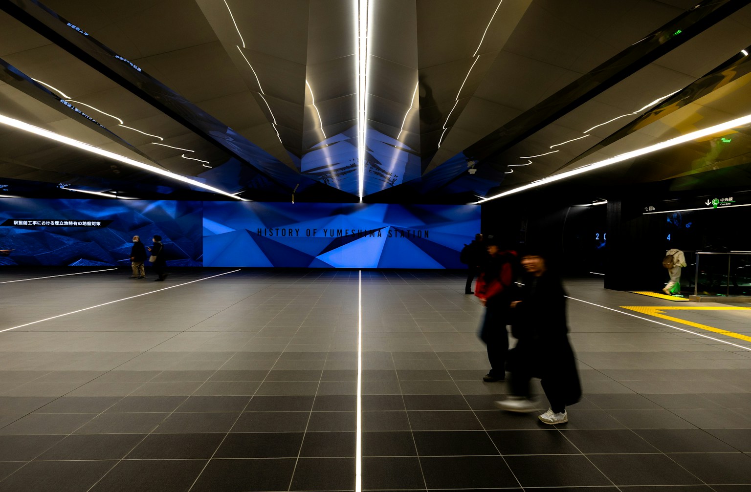 Intérieur moderne d'une station de métro avec un mur géométrique bleu et un sol carrelé spacieux avec des personnes marchant