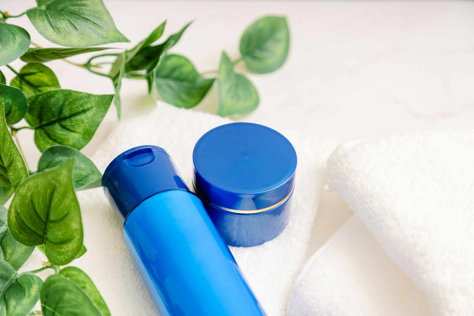 Image présentant des produits de soins de la peau bleus et des serviettes avec de la verdure en arrière-plan