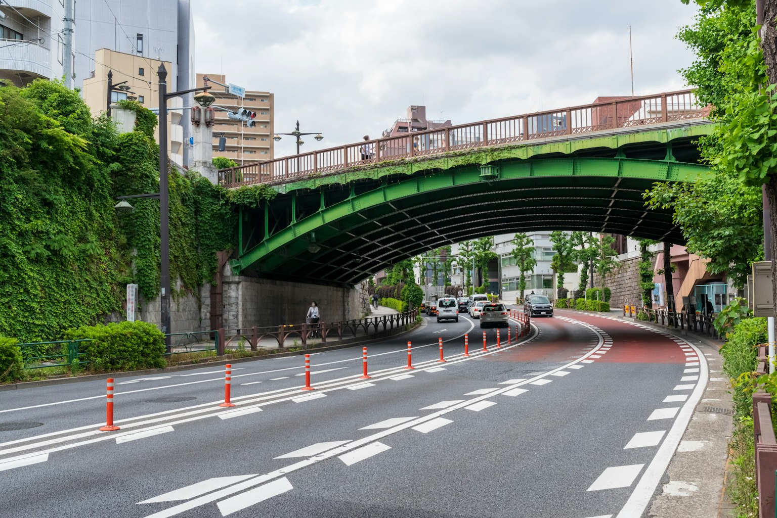 Scène de route avec des véhicules passant sous un pont en arc vert et des cônes de circulation