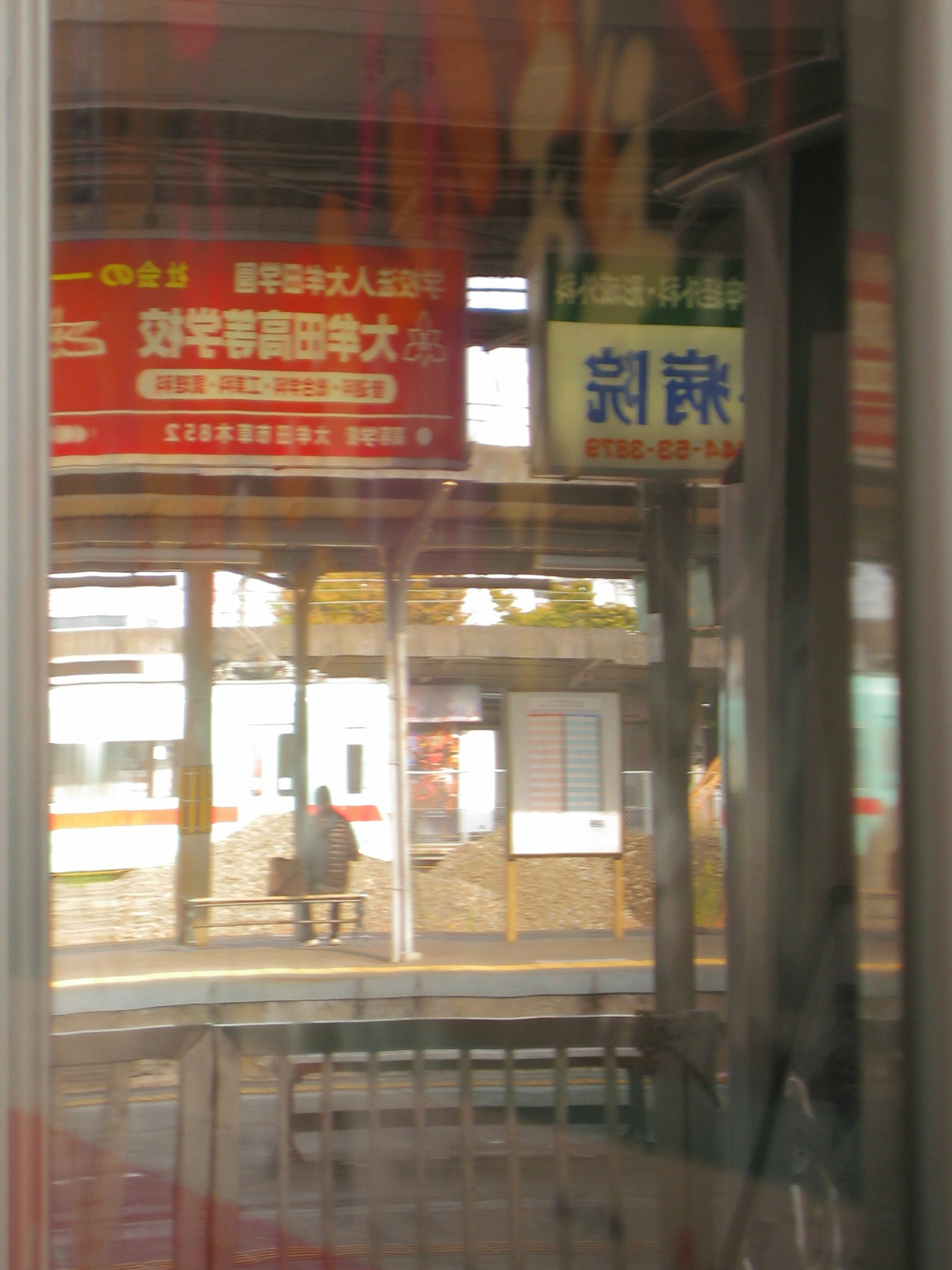 駅のホームに座る人の反射がある窓の外の風景