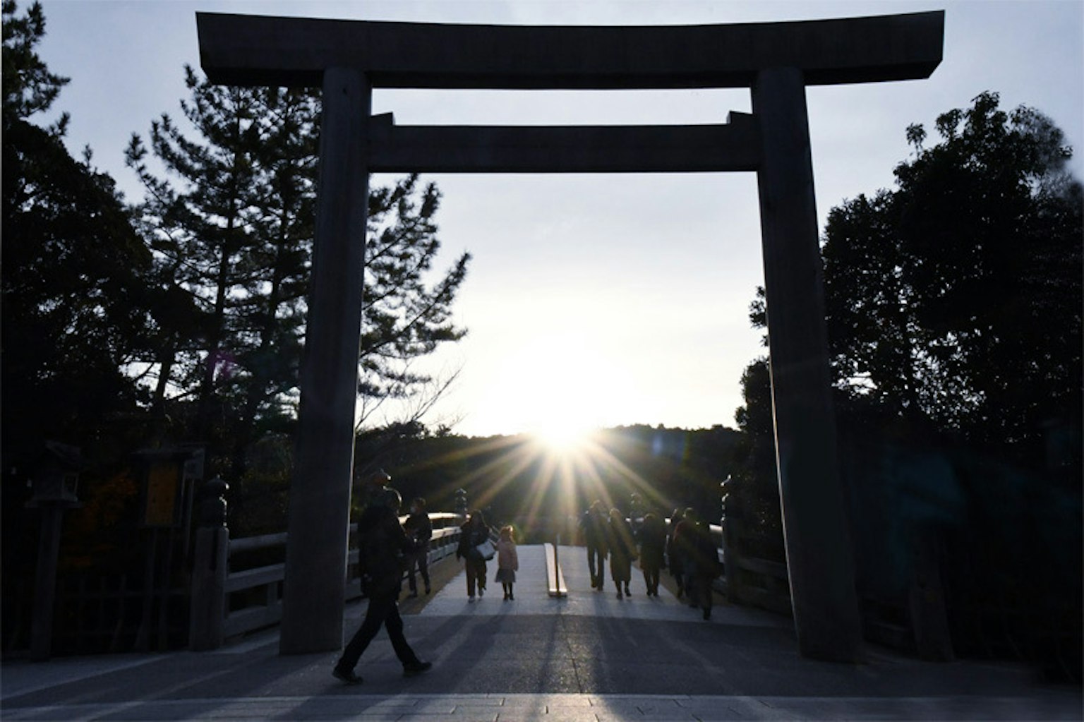Silhouette orang-orang yang lewat di bawah gerbang torii dengan latar belakang matahari terbenam