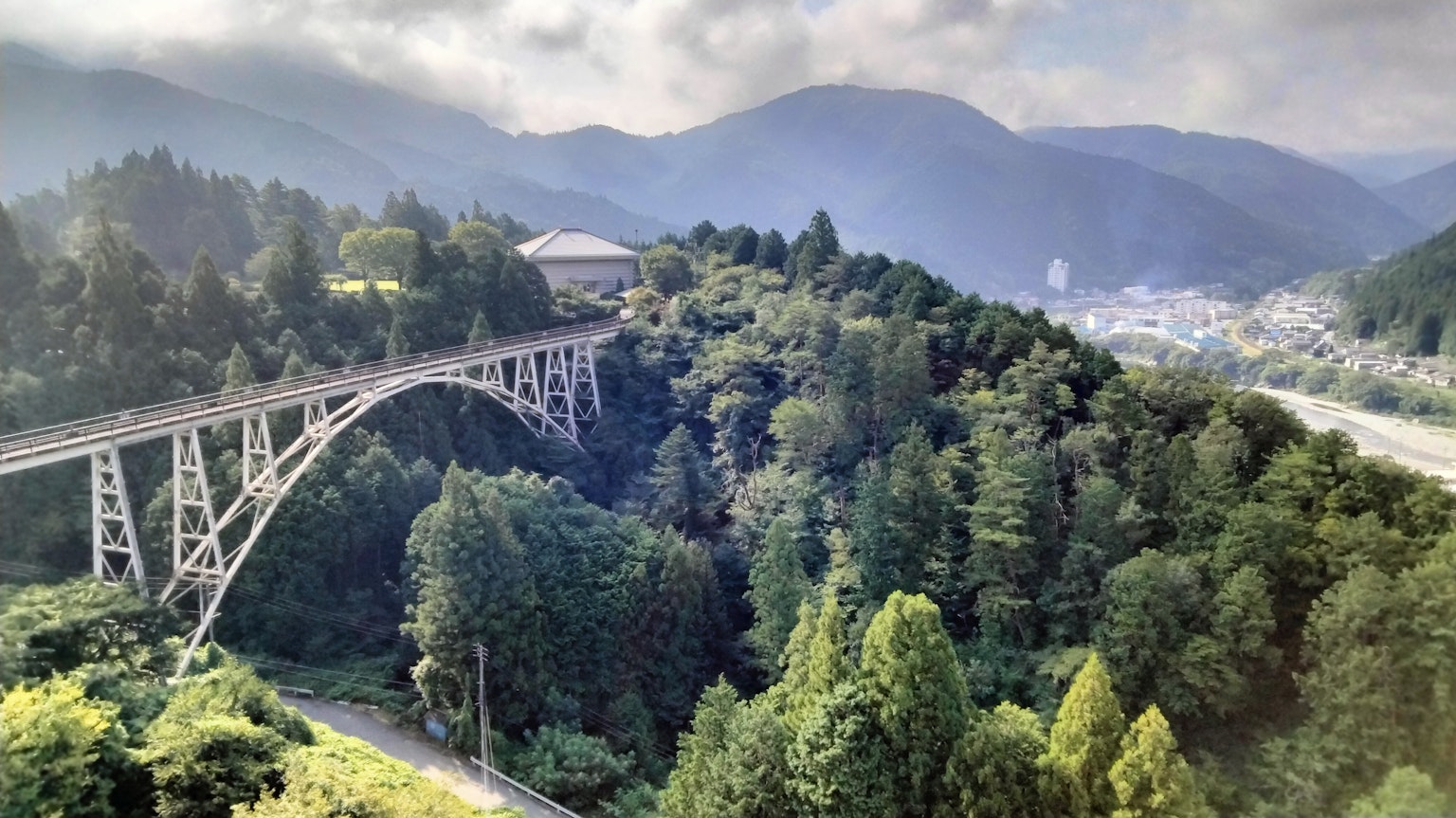 Eine malerische Aussicht auf eine Stahlbrücke, die grüne Berge und einen Fluss überspannt
